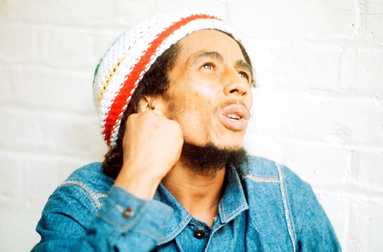 Bob Marley looks off-camera. He wears a denim shirt and knit rasta-colored headwear in 1975