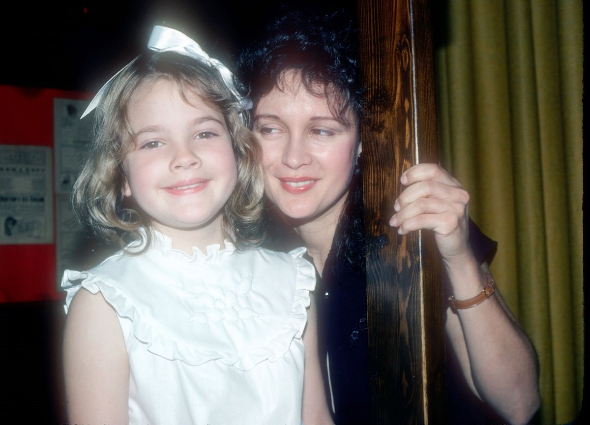 Drew Barrymore as a child in a white dress and bow with her mother, Jaid.