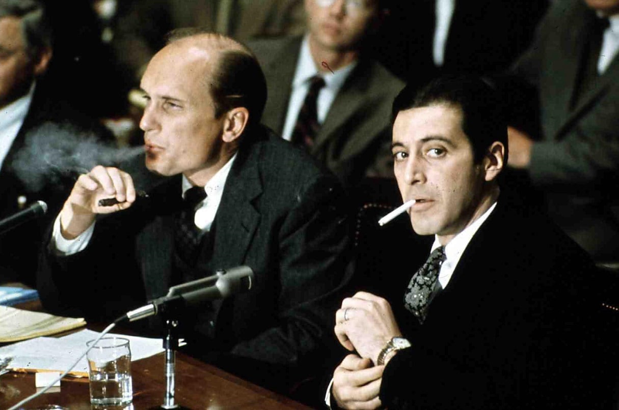 Robert Duvall and Al Pacino in suits, seated at a table with microphones in front of them, as Tom Hagen and Michael Corleone  in 'The Godfather: Part II'
