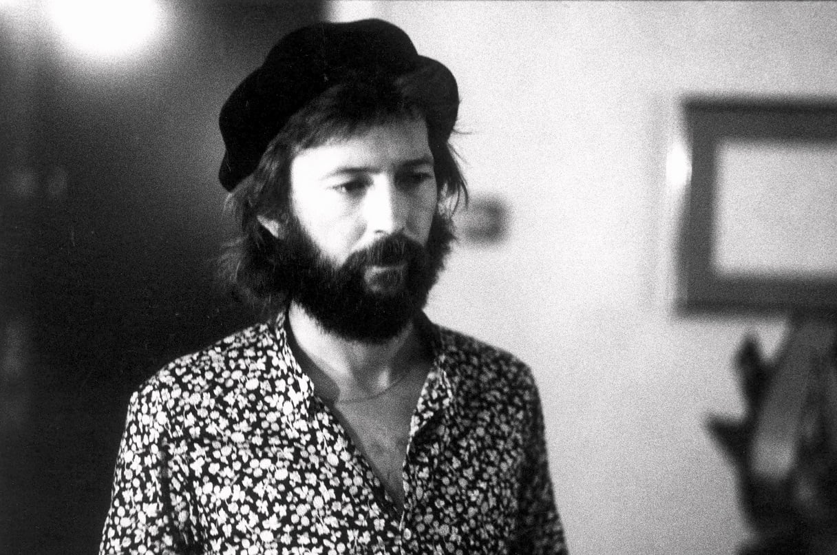 A bearded Eric Clapton in a floral-patterned shirt and hat backstage in 1974