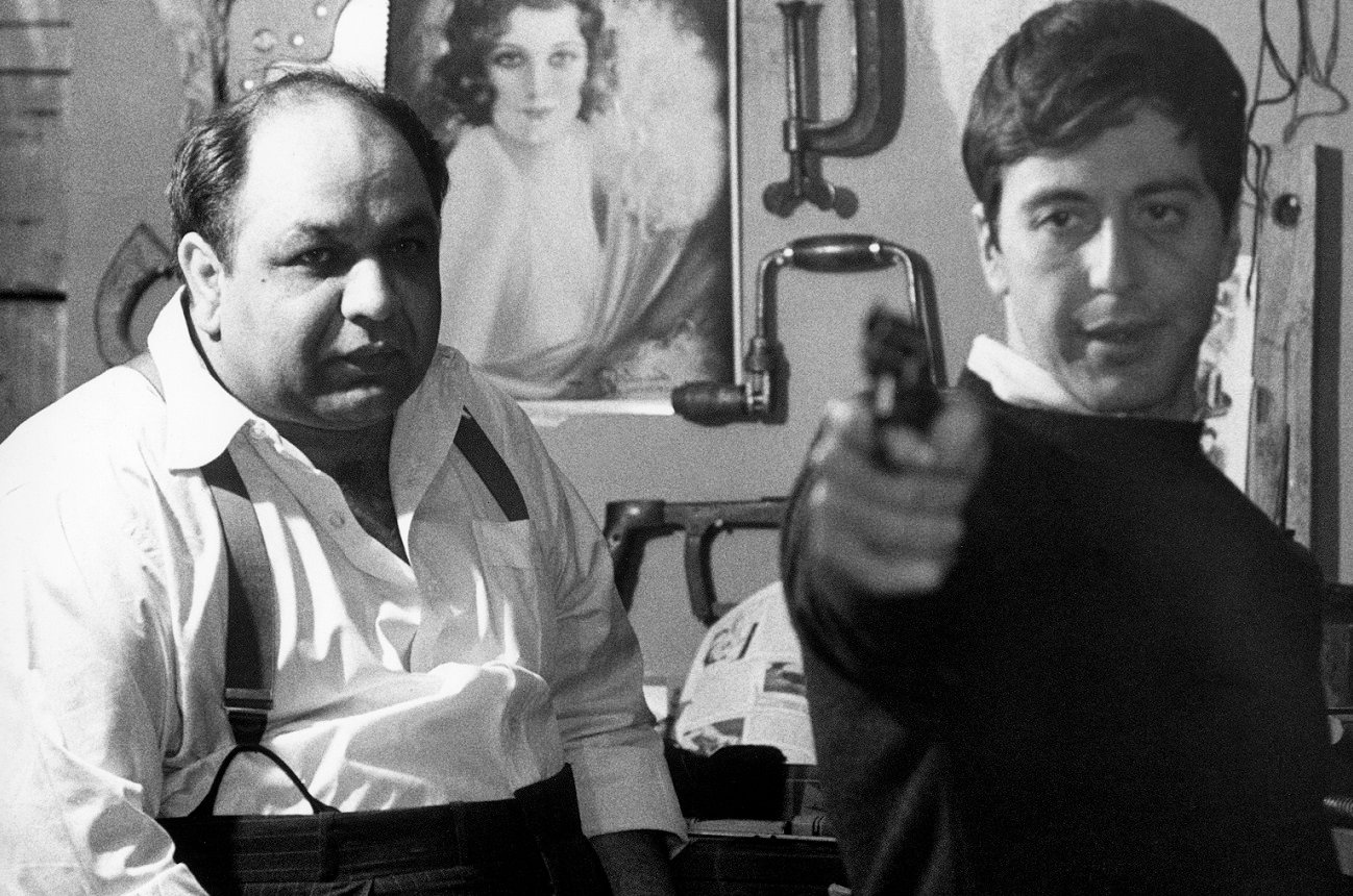 Al Pacino points a gun toward the camera as Richard Castellano looks on in a scene from 'The Godfather'