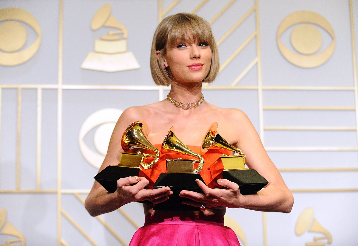 Taylor Swift in a pink dress holding three Grammy Awards