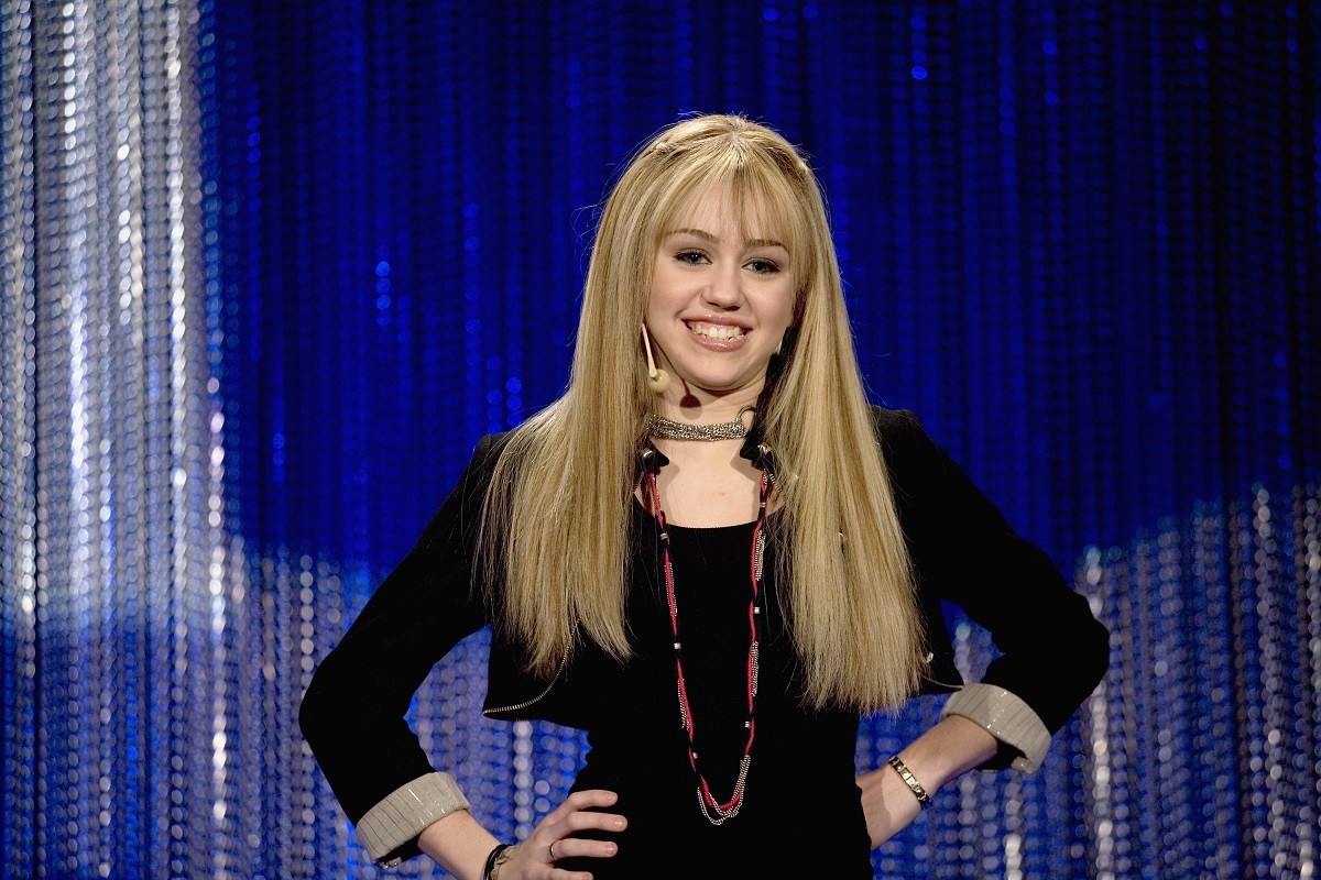 Miley Cyrus in a blonde wig with her hands on her hips