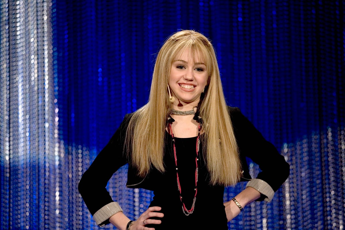 Miley Cyrus in a blonde wig for 'Hannah Montana' with her hands on her hips