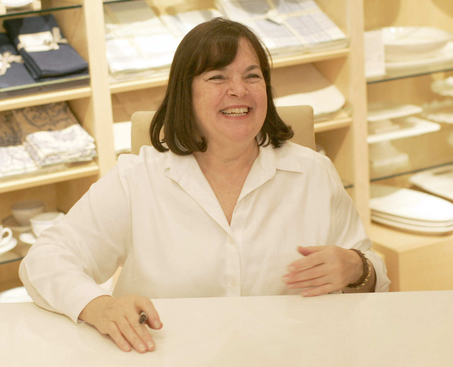 Ina Garten smiles as she sits at a table during a book signing at William Sonoma