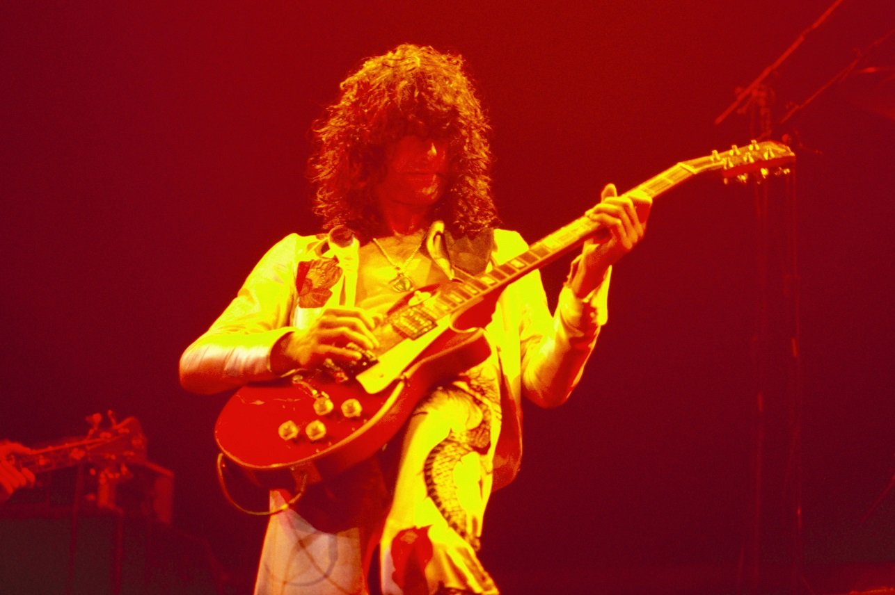 Jimmy Page playing guitar bathed in orange light on stage
