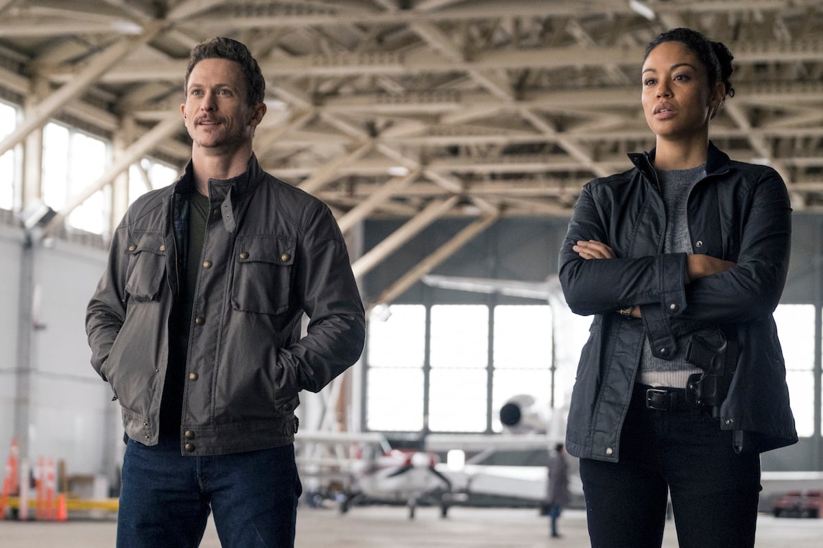 Bryan and Finola standing next to each other in an airplane hanger in Debris series premiere 