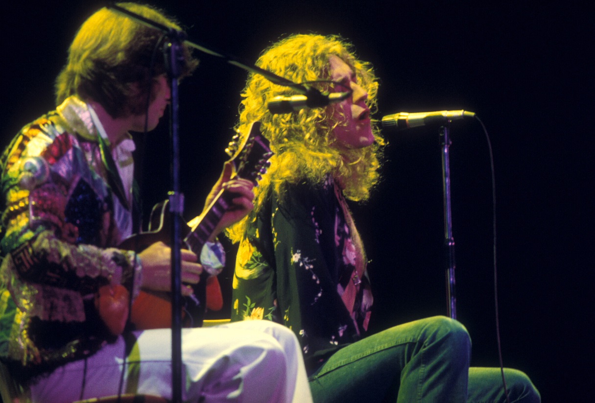 John Paul Jones plays mandolin in a multi-colored jacket as Robert Plant sings in a flowing, open black shirt in 197