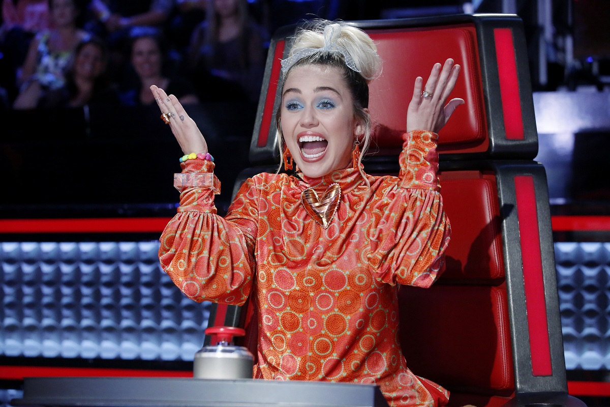 Miley Cyrus in a red chair on 'The Voice' with her hands in the air