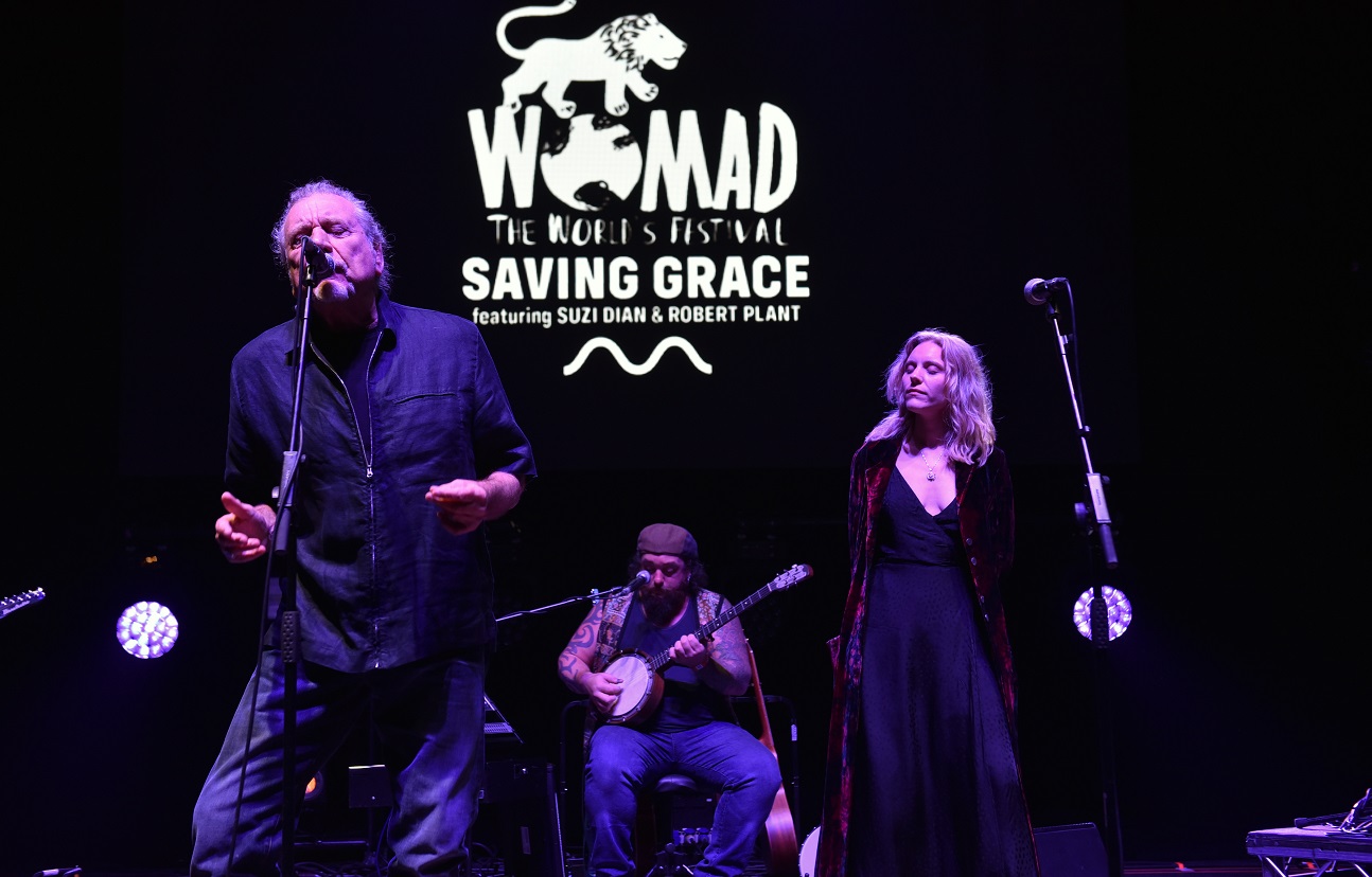 Robert Plant sings with Suzi Dian standing to his left and a member of Saving Grace performing on banjo behind them