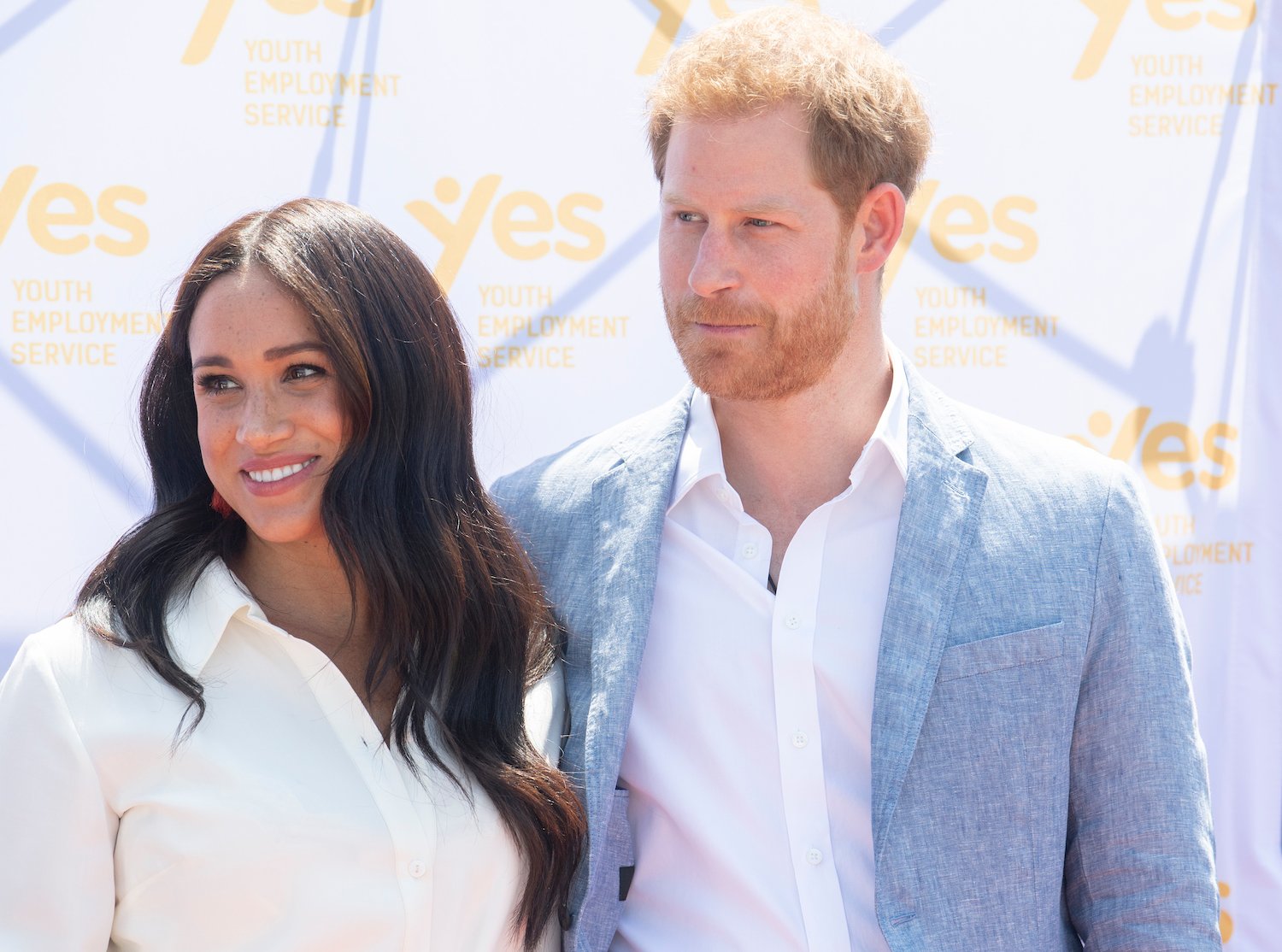 Meghan Markle wearing a white dress, posing next to Prince Harry