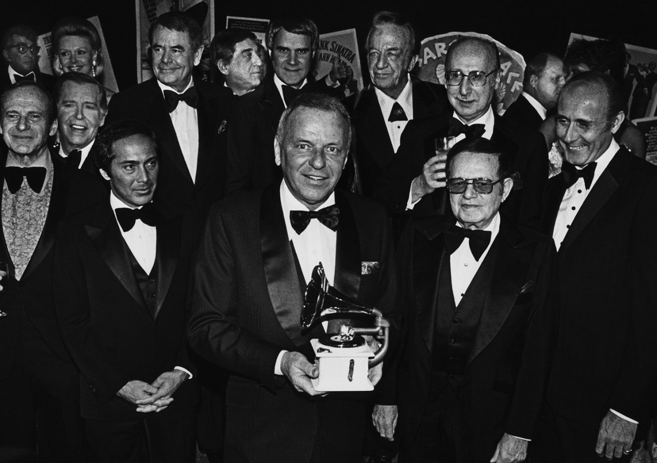 1979: Frank Sinatra holds a Grammy Award surrounded by celebrity friends. Paul Anka stands to his right.