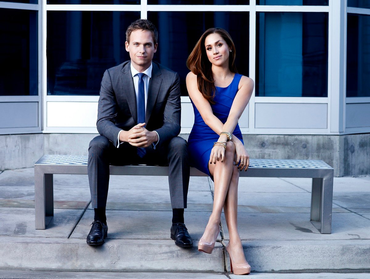 Patrick J. Adams and Meghan Markle sitting on a bench in a promo shoot for 'Suits'