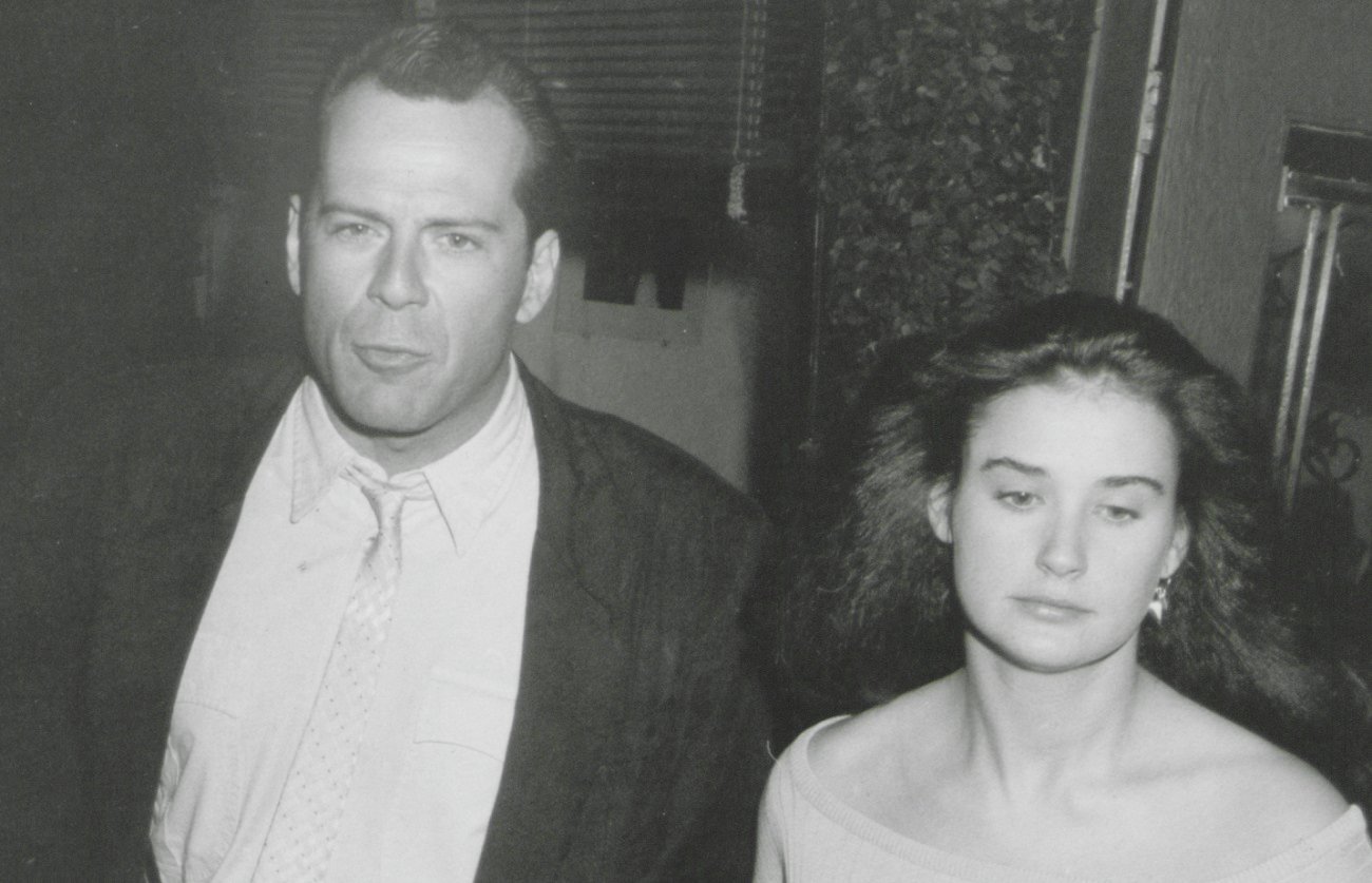 Bruce Willis wears a suit and looks at the camera while Demi Moore averts her eyes in a 1985 black-and-white photo