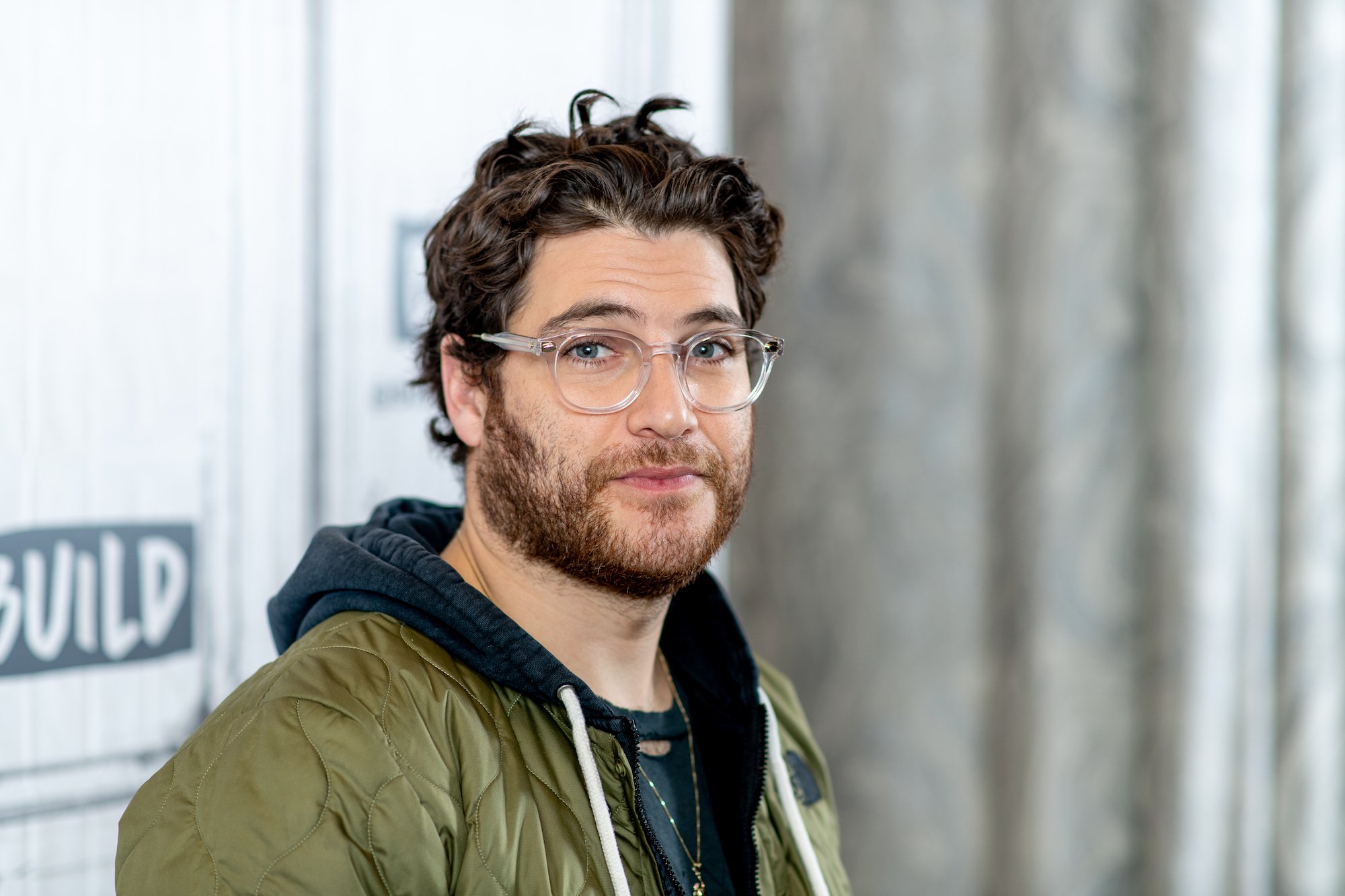 Adam Pally smiling in front of a gray background