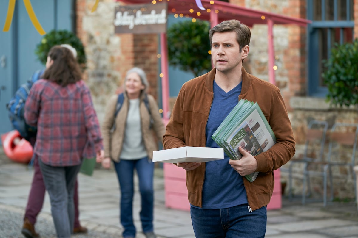 Allen Leech standing on the street and holding a box in As Luck Would Have It 