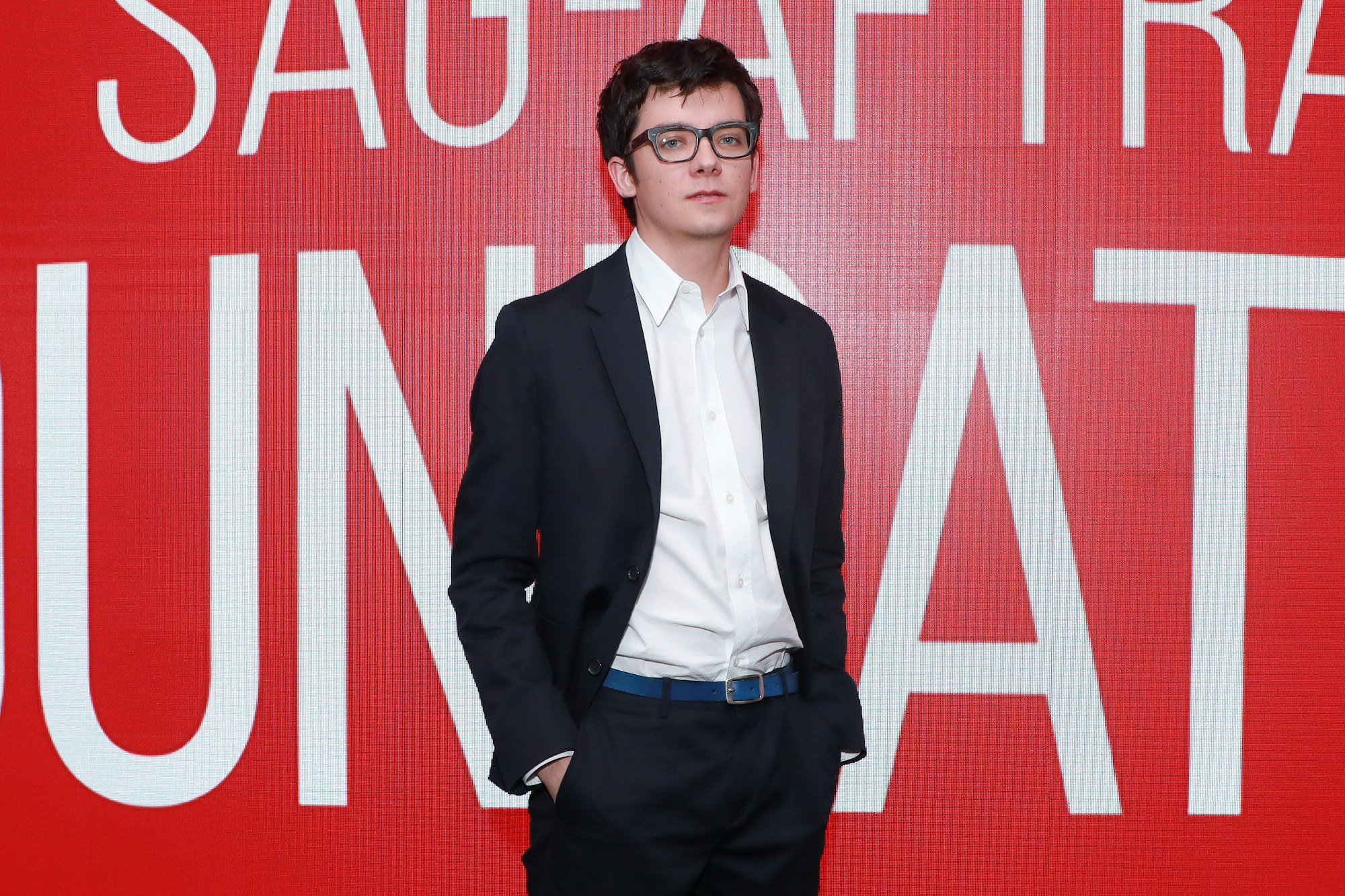 Asa Butterfield in front of a red background