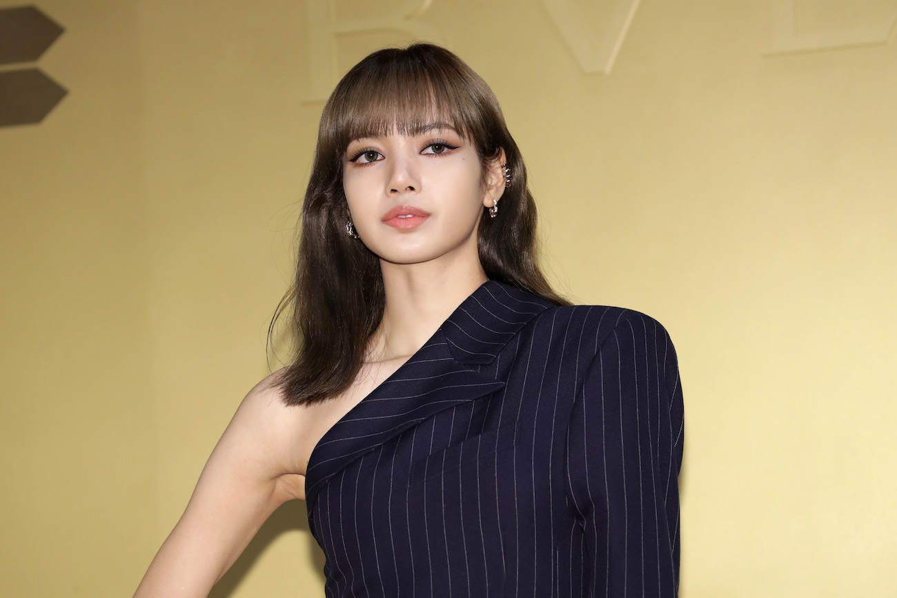 BLACKPINK's Lisa posing in black outfit in front of a yellow backdrop