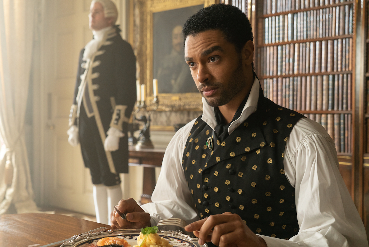 REGÉ-JEAN PAGE as SIMON BASSET is sitting a desk and raising his eyebrow in 'Bridgerton'