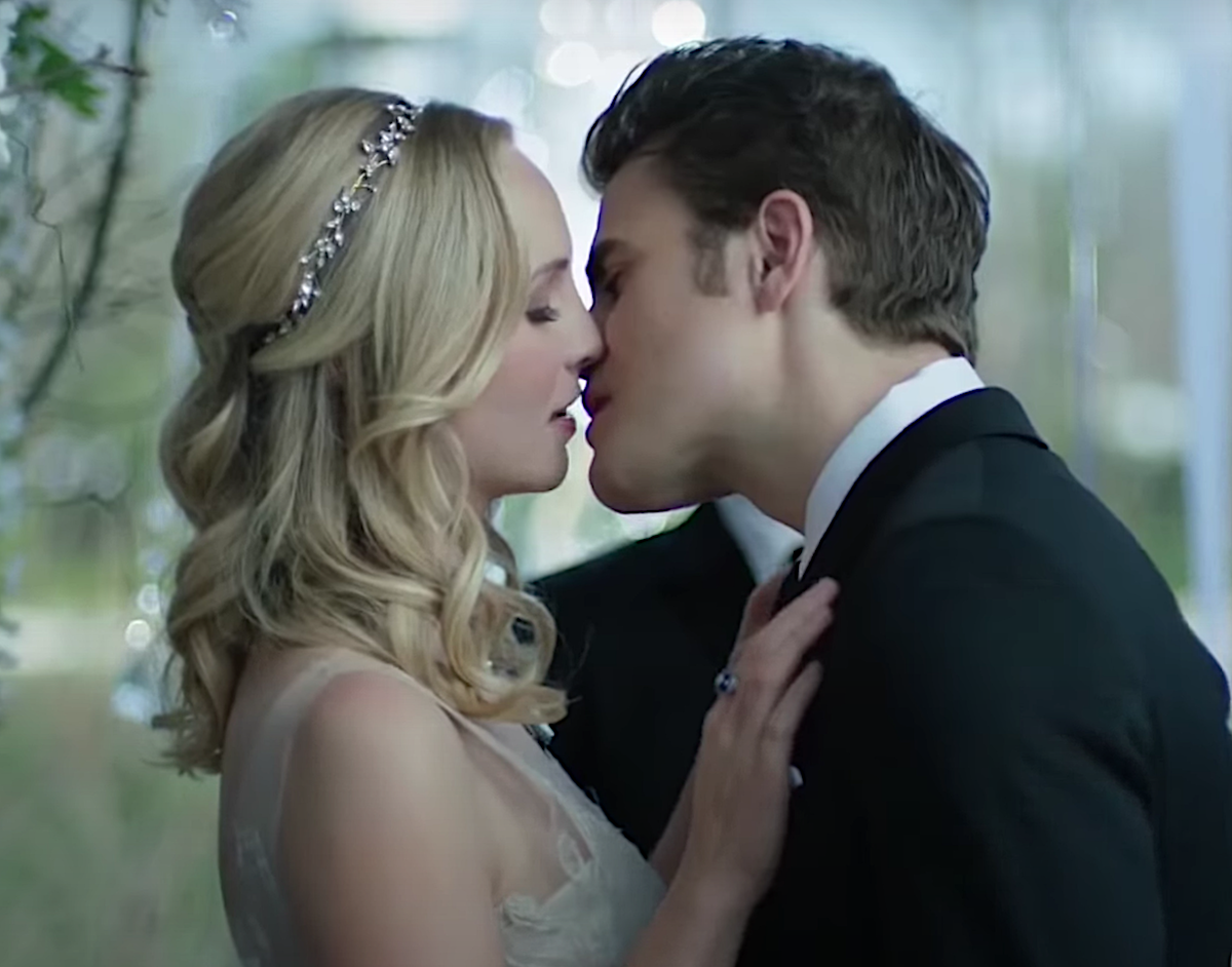 Candice King in a wedding dress and Paul Wesley in a tux lean in for a kiss at a wedding altar as Caroline Forbes as Stefan Salvatore in 'The Vampire Diaries'