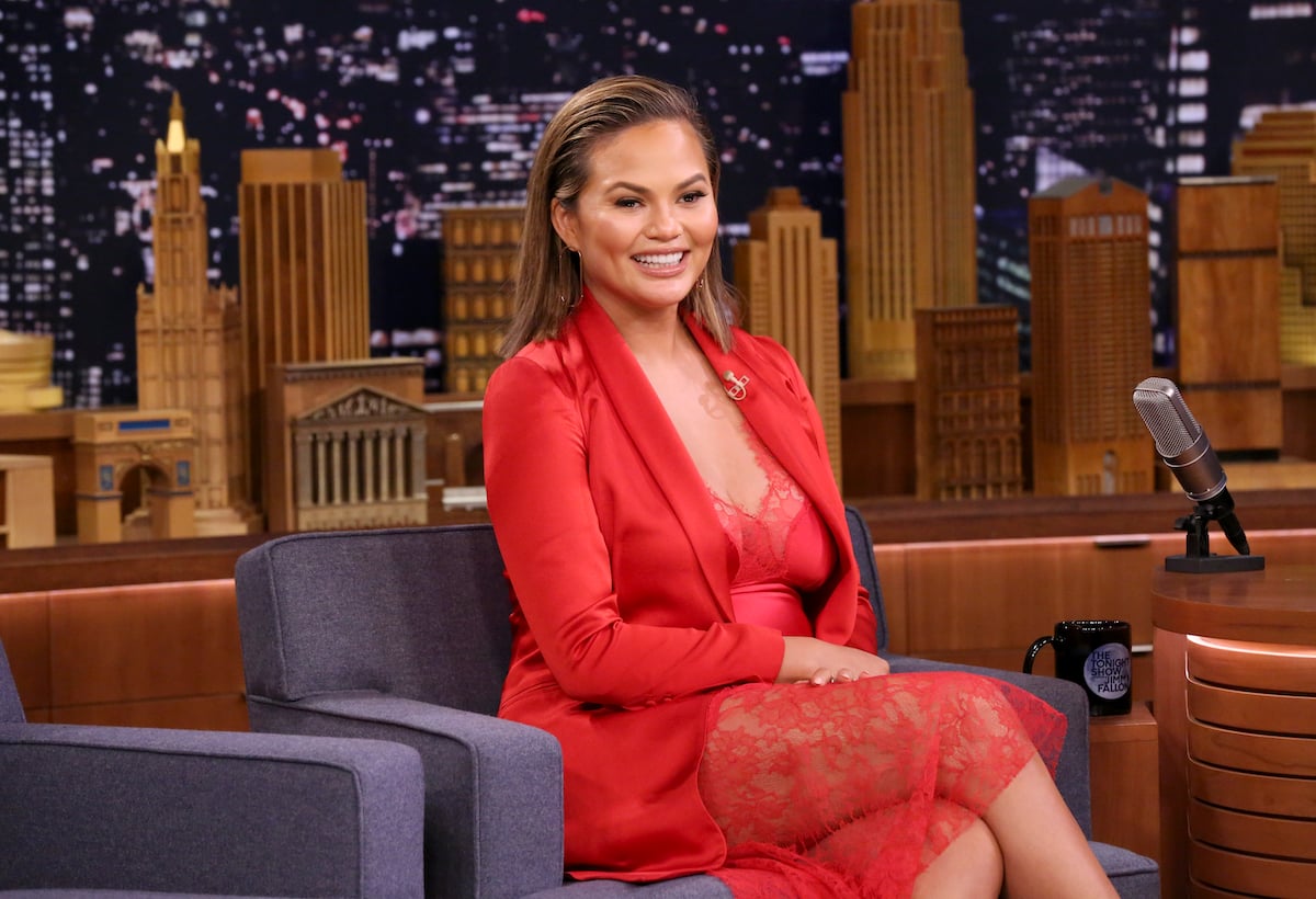 Model/Actress Chrissy Teigen wearing red and sitting in a chair smiling