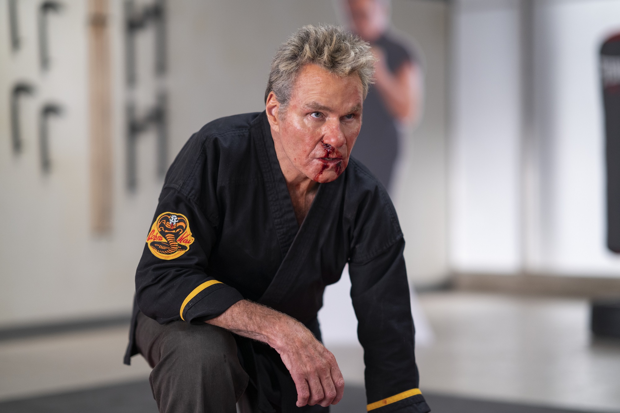 Cobra Kai Sensei Kreese kneels with a bloody nose