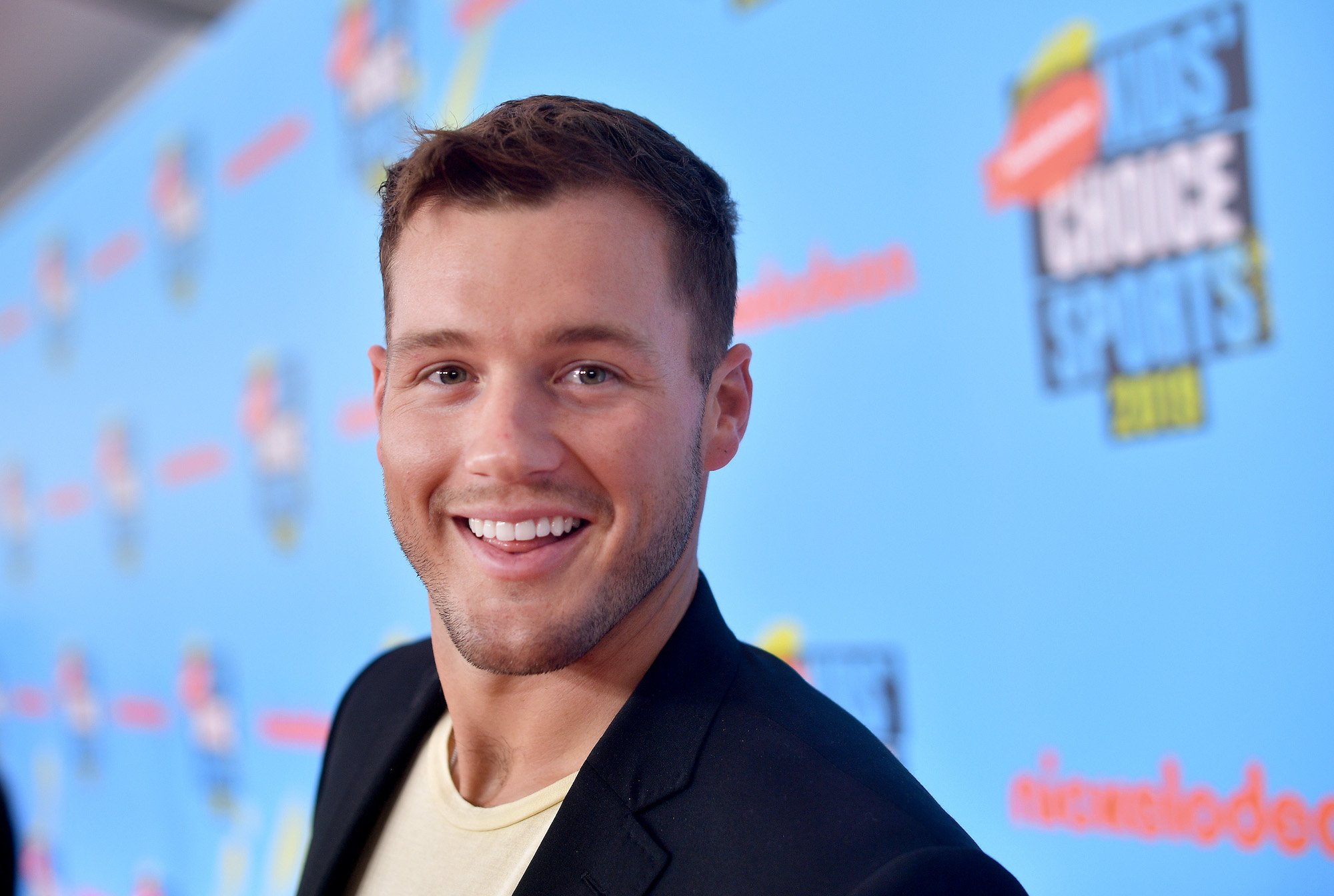 Colton Underwood smiling in front of a blue background