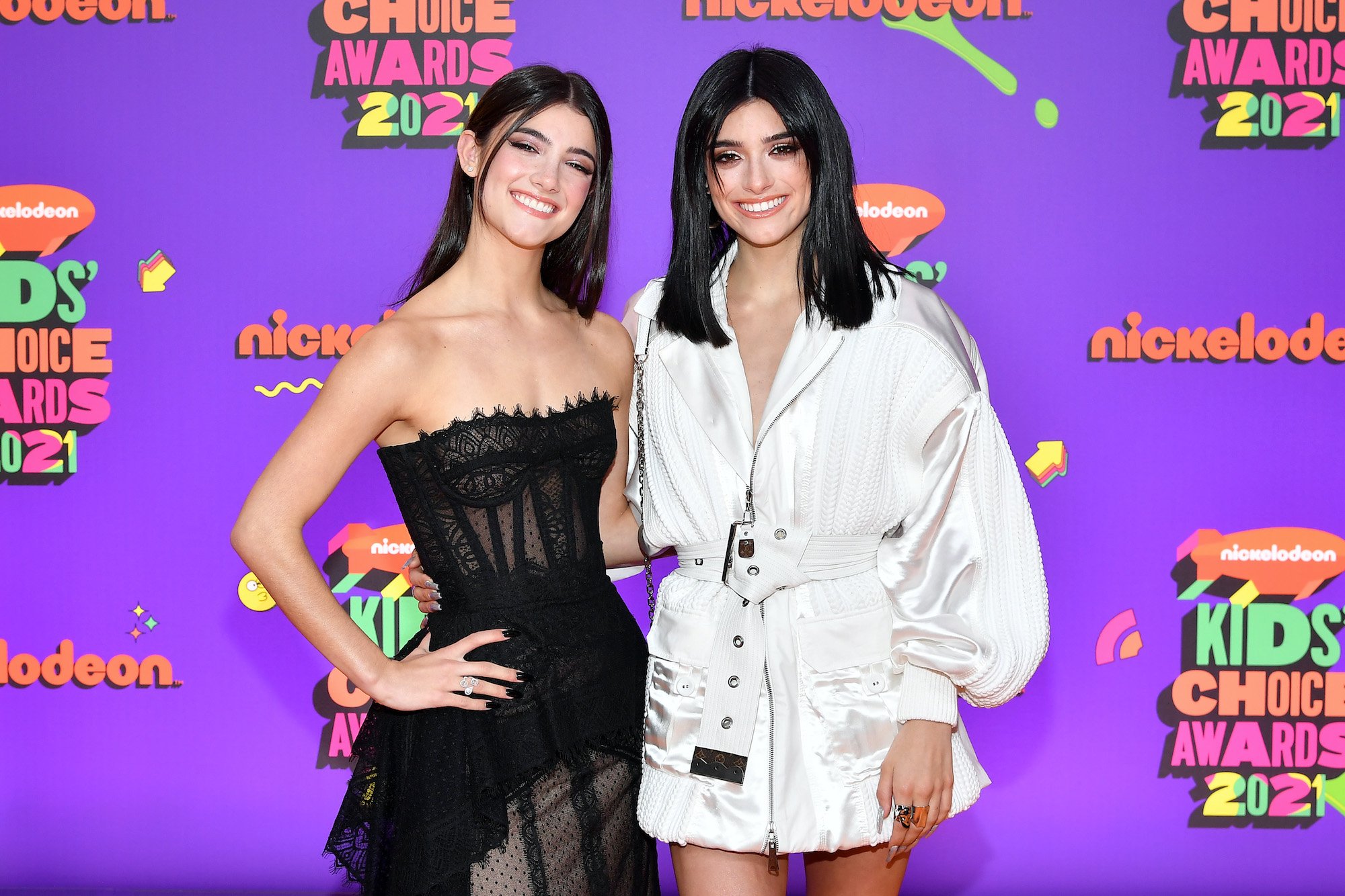 (L-R) Charli D'Amelio and Dixie D'Amelio smiling in front of a purple background