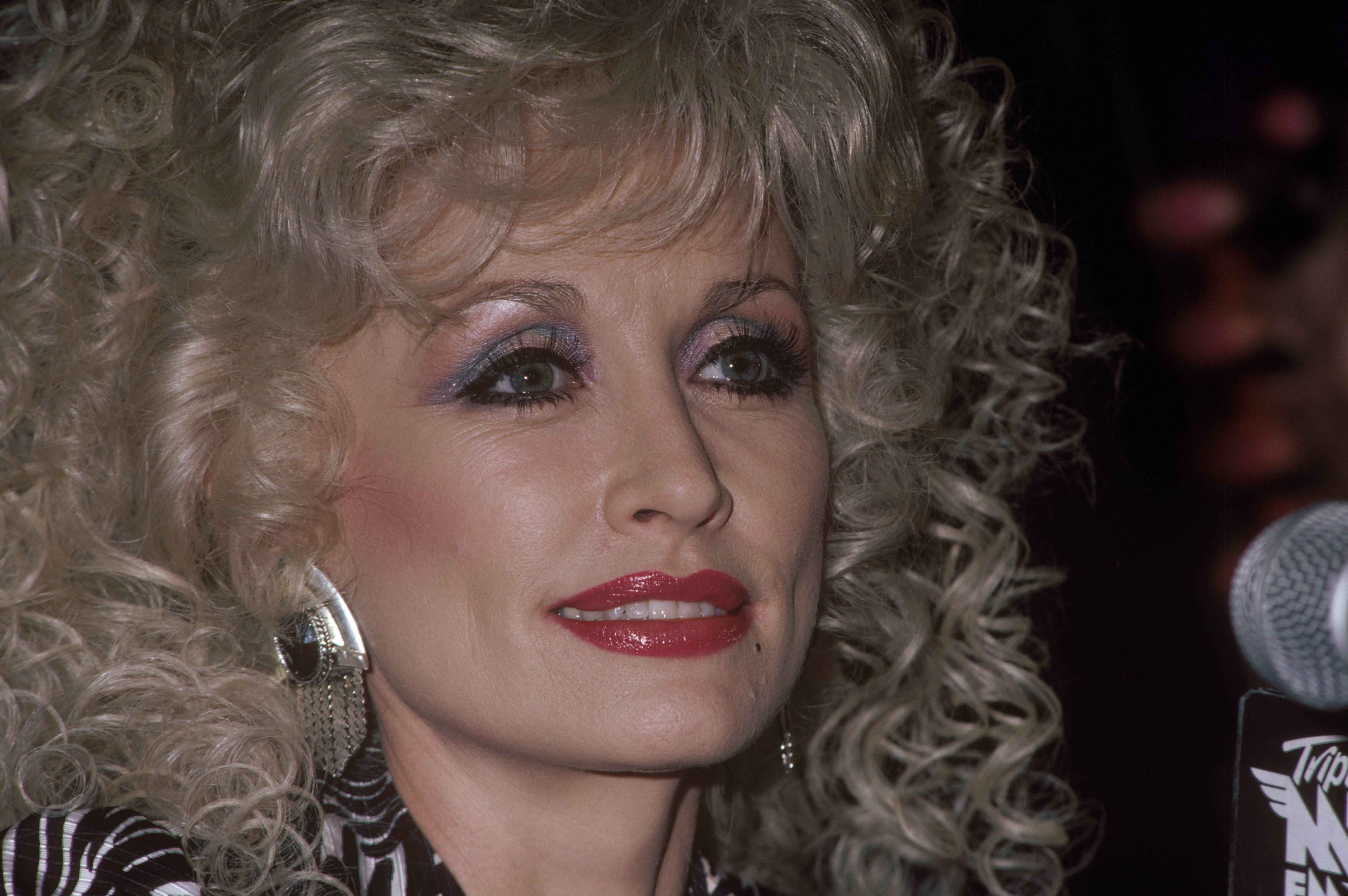 A close-up of Dolly Parton. She has her hair and makeup done in the style of the '80s.
