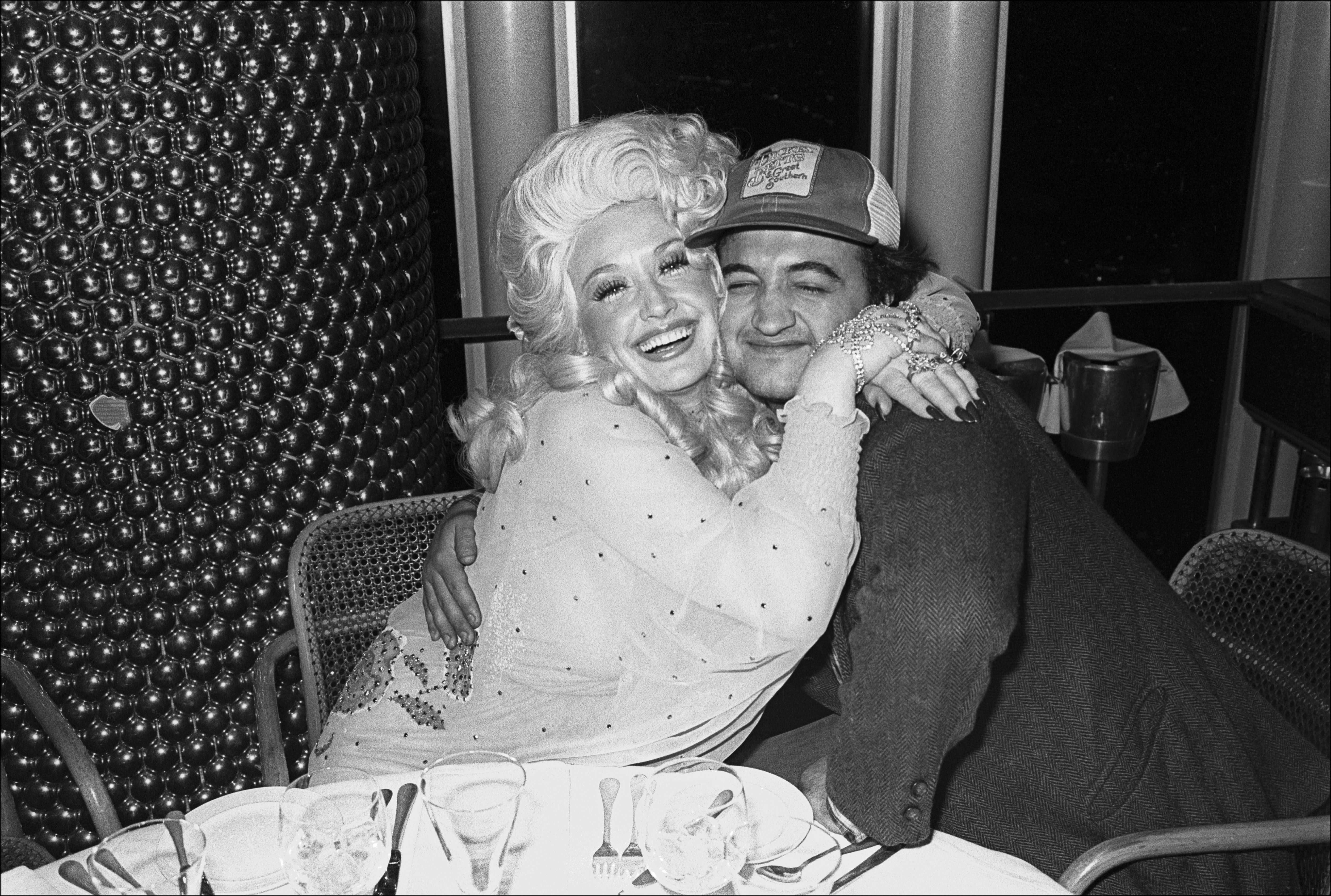 Dolly Parton and comedian John Belushi hug as they pose together at the Windows on the World restaurant.