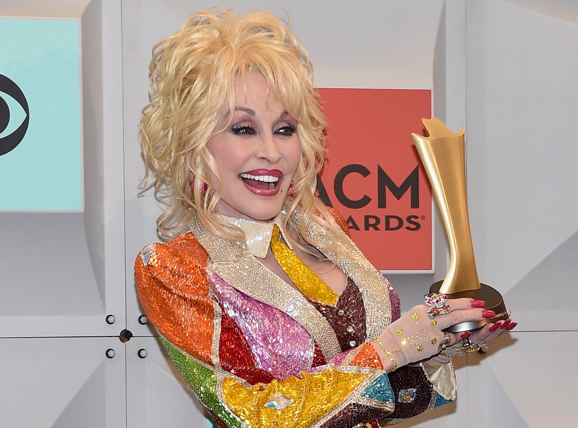 Dolly Parton dressed in a colorful blazer and holding her award backstage at the 51st Academy of Country Music Awards