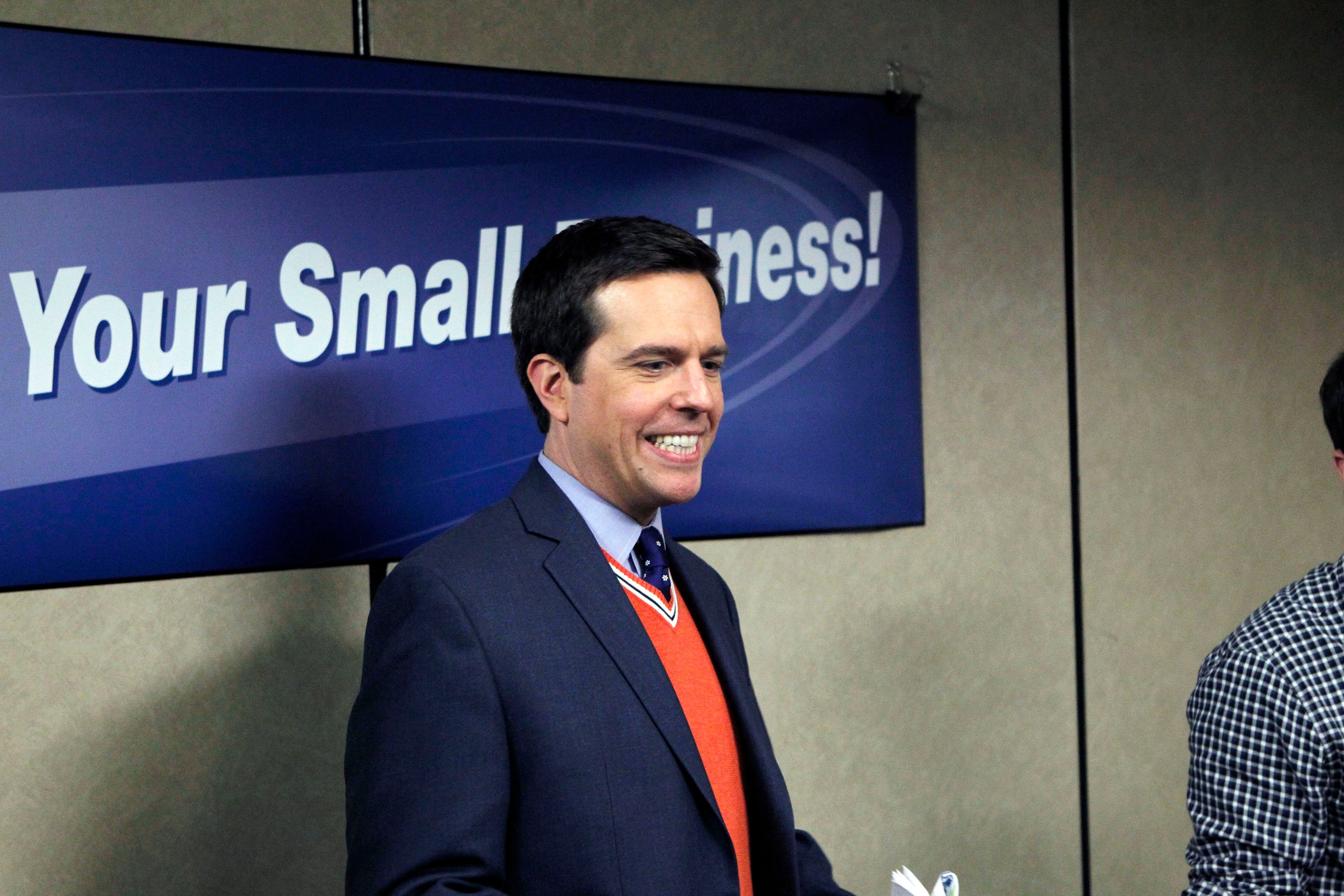 Ed Helms in a blue jacket and orange vest in a scene from 'The Office'