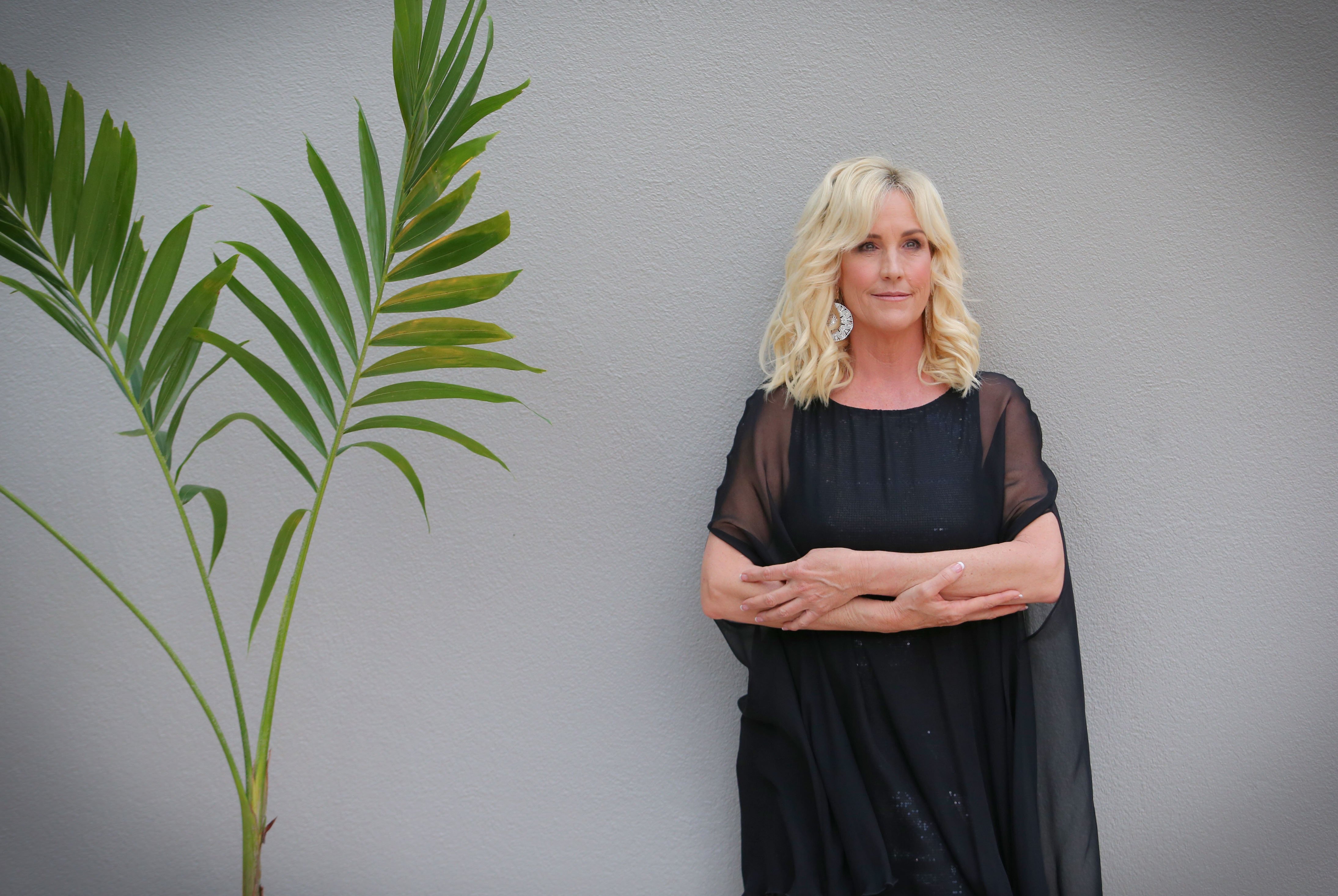 Activist Erin Brokovich in a black dress standing against a gray wall