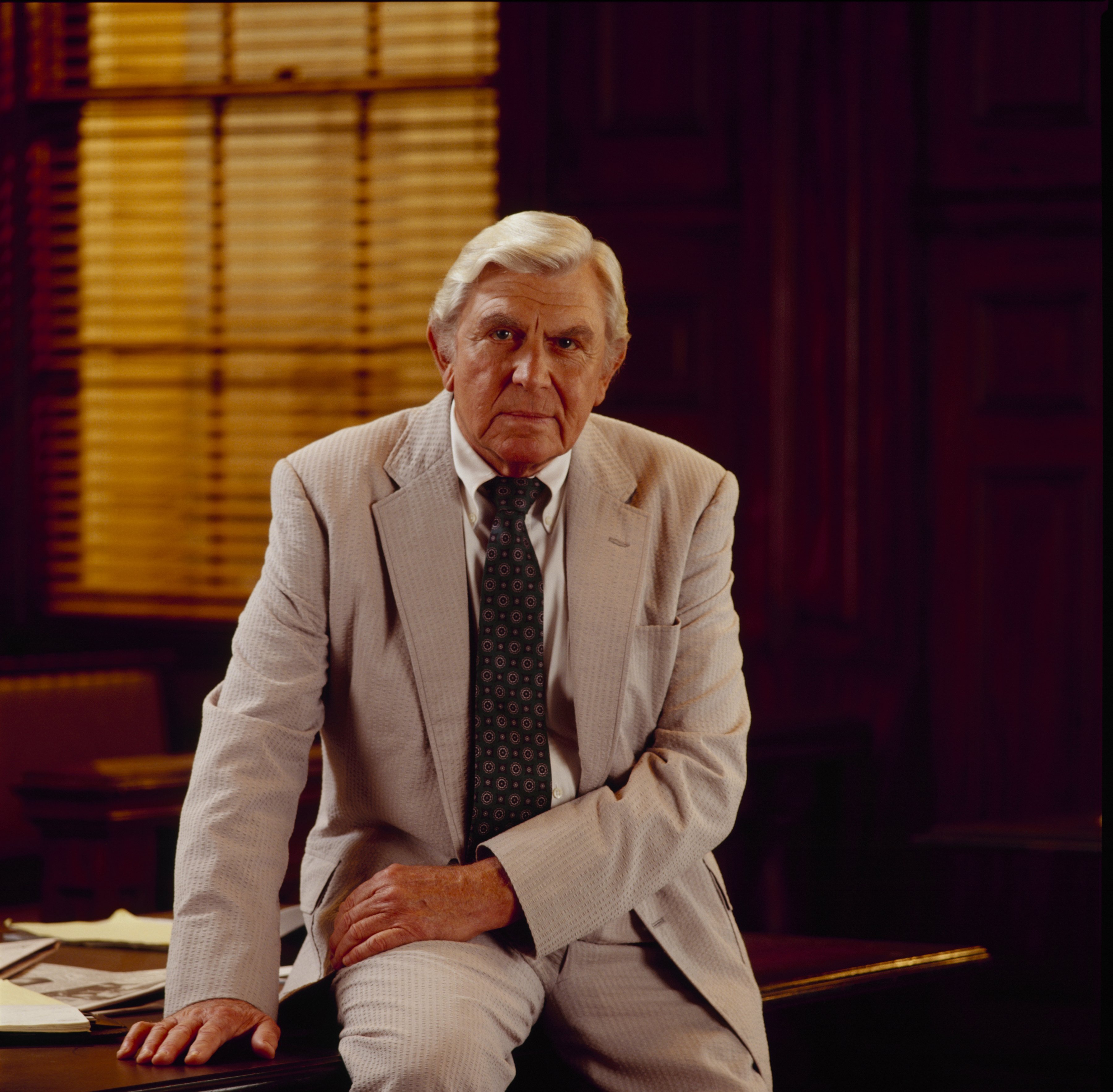 Andy Griffith is photographed seated on the edge of a desk in a light-colored suit as Ben Matlock, lead character of the legal drama 'Matlock,' 1992