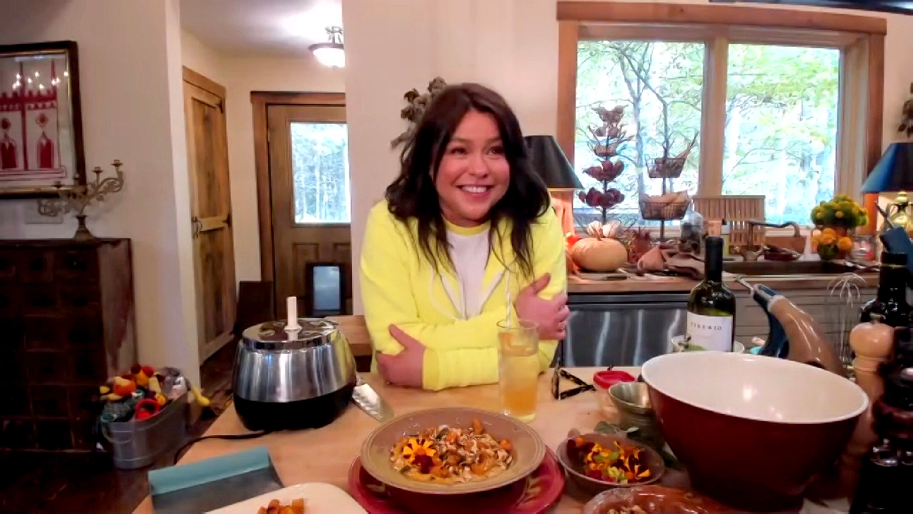 Rachael Ray poses during Food Network's 'In the Kitchen With Rachael Ray' in a sunny yellow sweater, while leaning on her kitchen counter.
