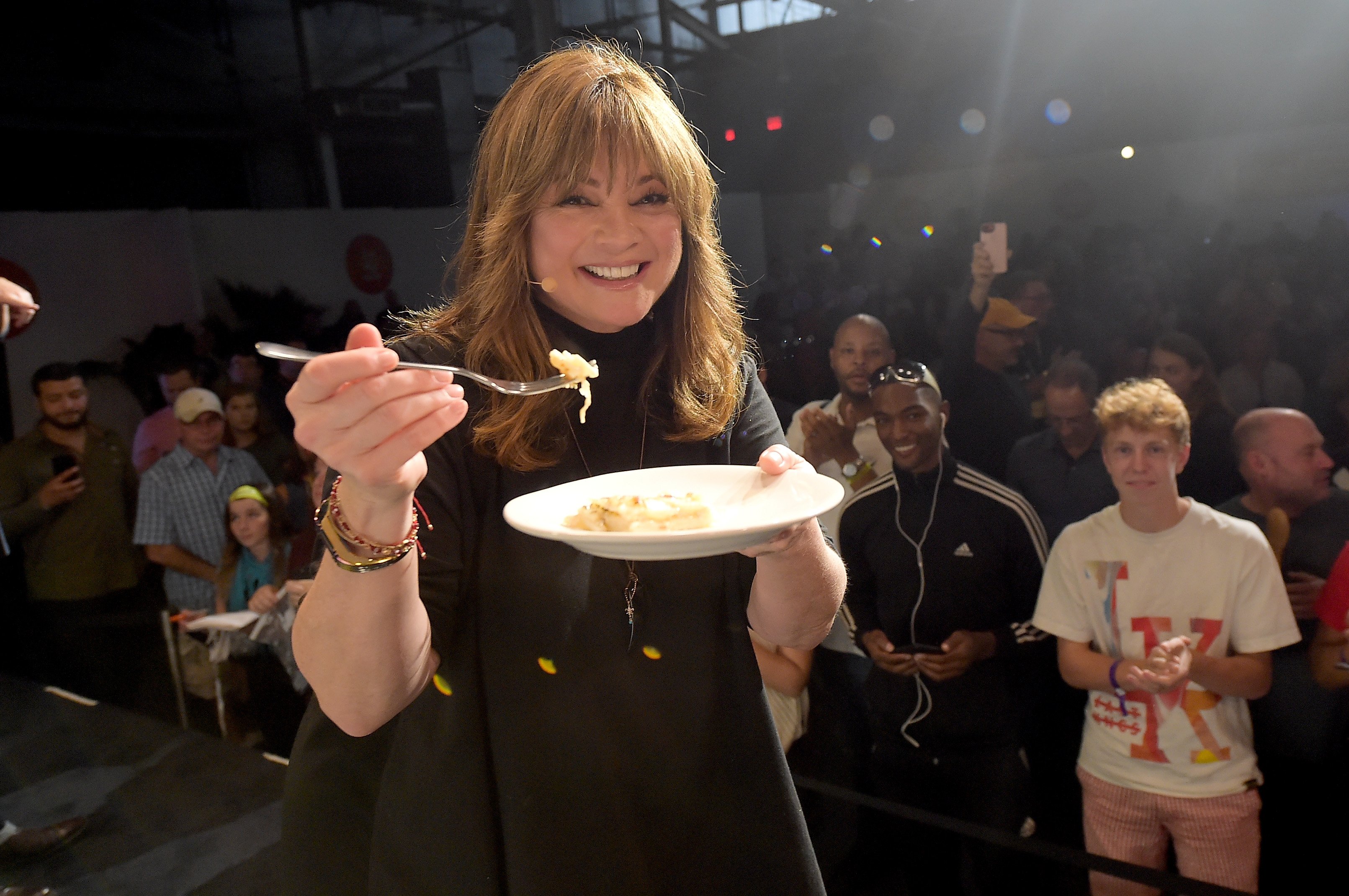 Valerie Bertinelli offers the camera a bite off her plate of food while an audience looks on at the 2017 Cooking Channel New York City Wine & Food Festival