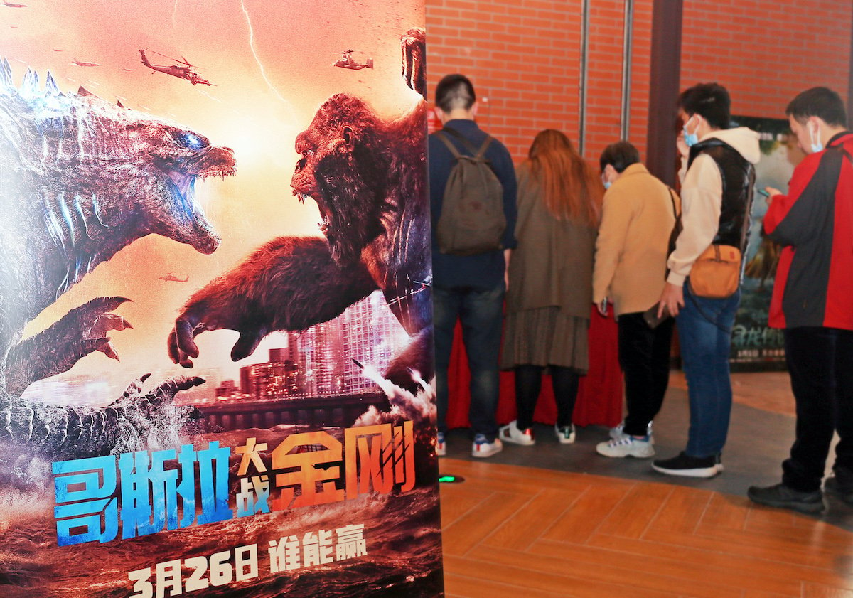 People in Shanghai, China stand beside a poster of 'Godzilla vs. Kong'