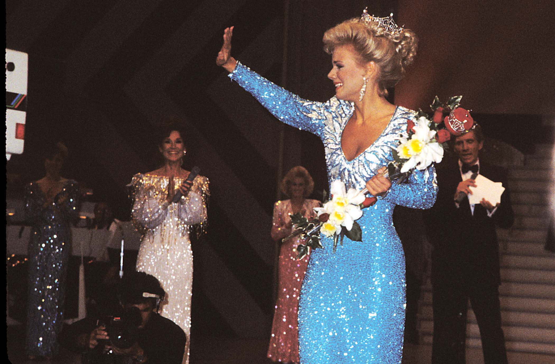 Gretchen Carlson wearing a blue dress and holding flowers at the Miss America pageant in 1988