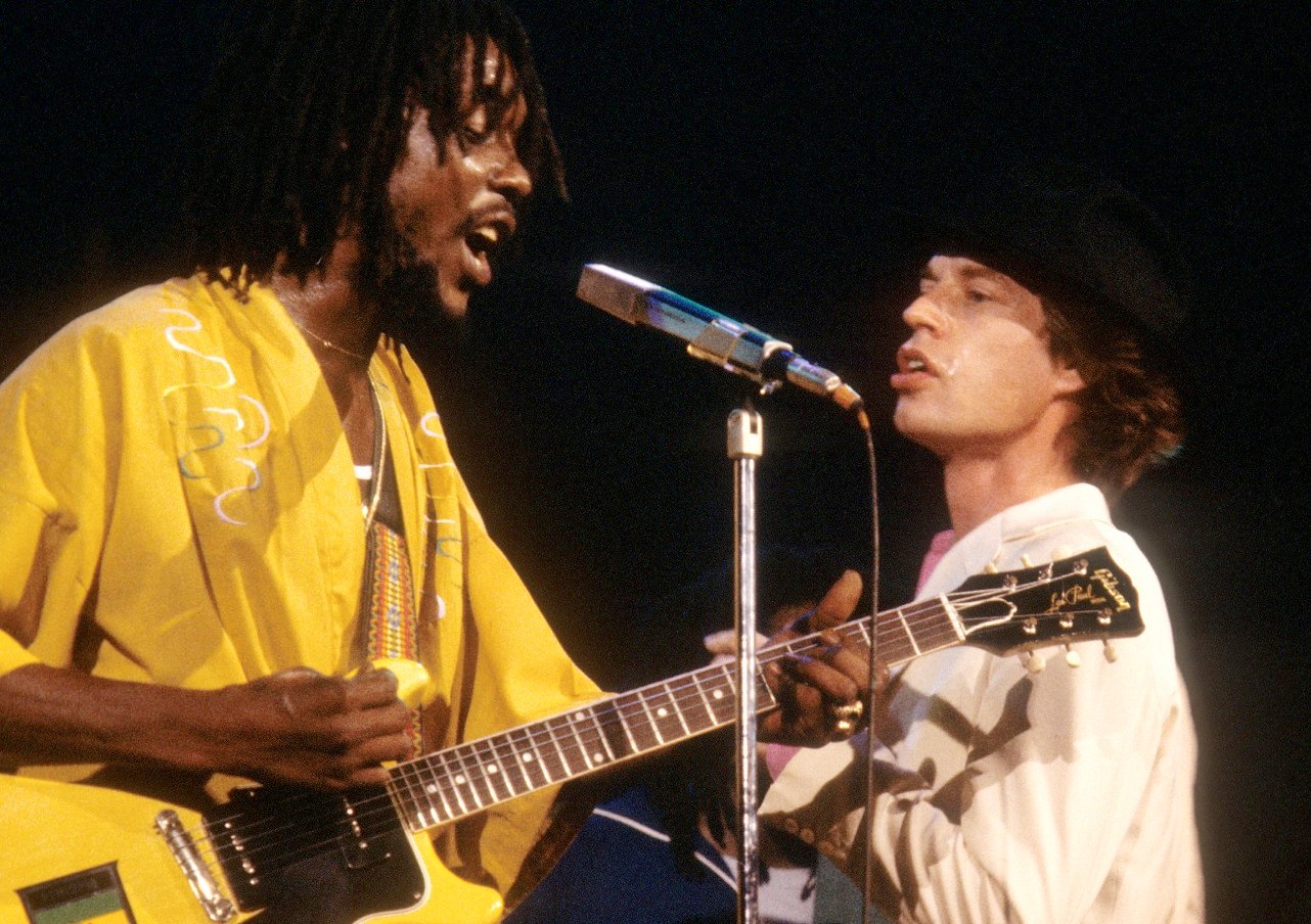 Peter Tosh sings on stage as Mick Jagger stands near the microphone