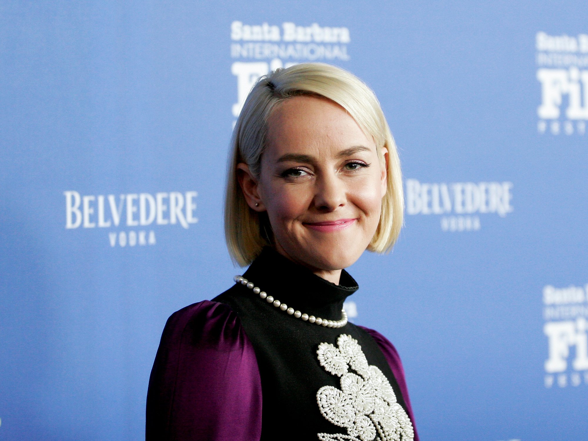 Jena Malone smiling in front of a blue background