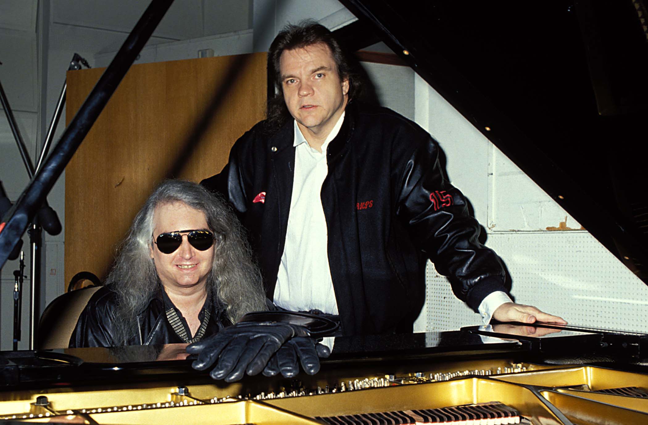 Jim Steinman sits at a piano while Meat Loaf stands