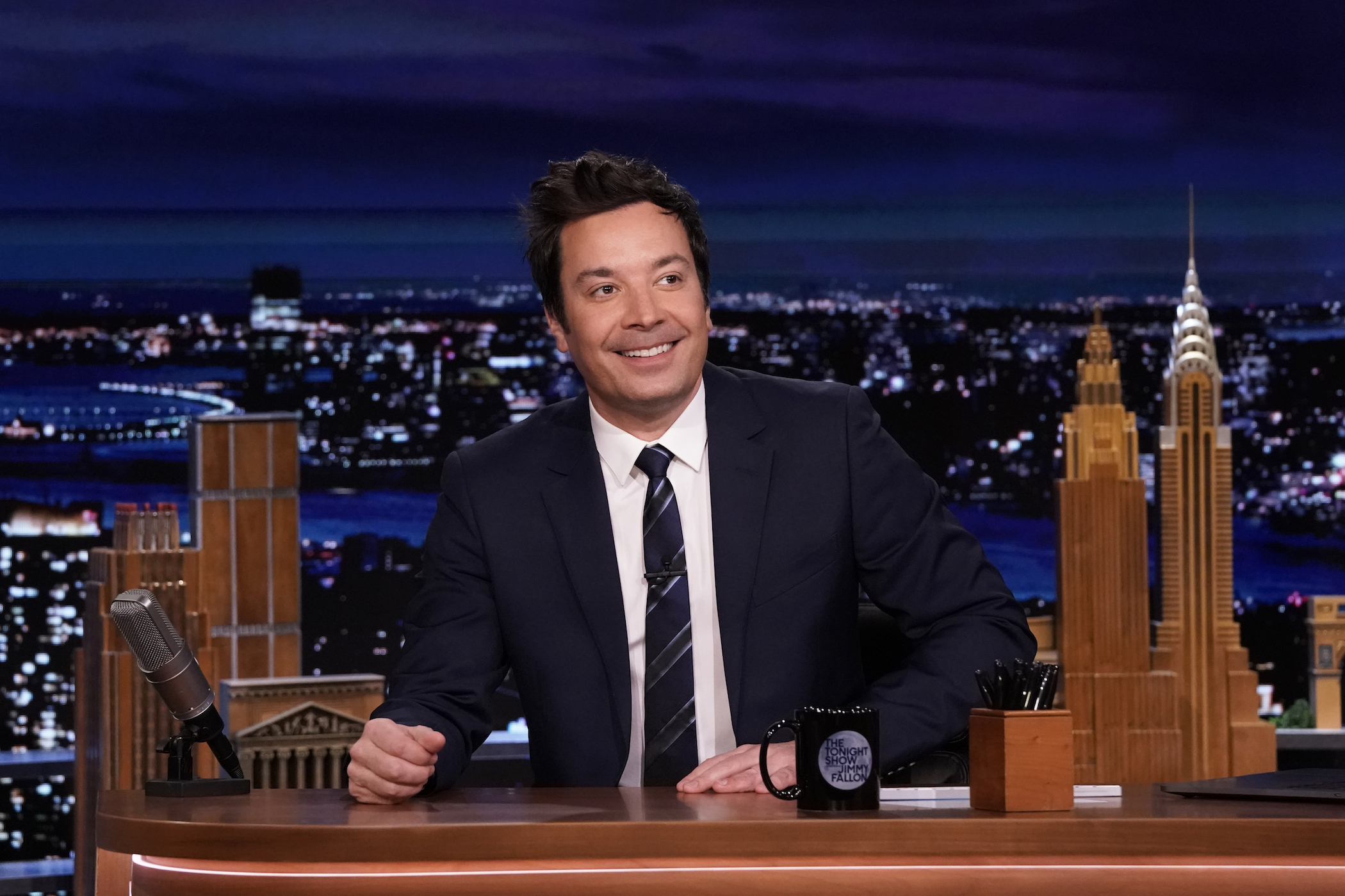 Jimmy Fallon smiling and sitting at his desk on 'The Tonight Show Starring Jimmy Fallon,' where he accrues an incredible net worth
