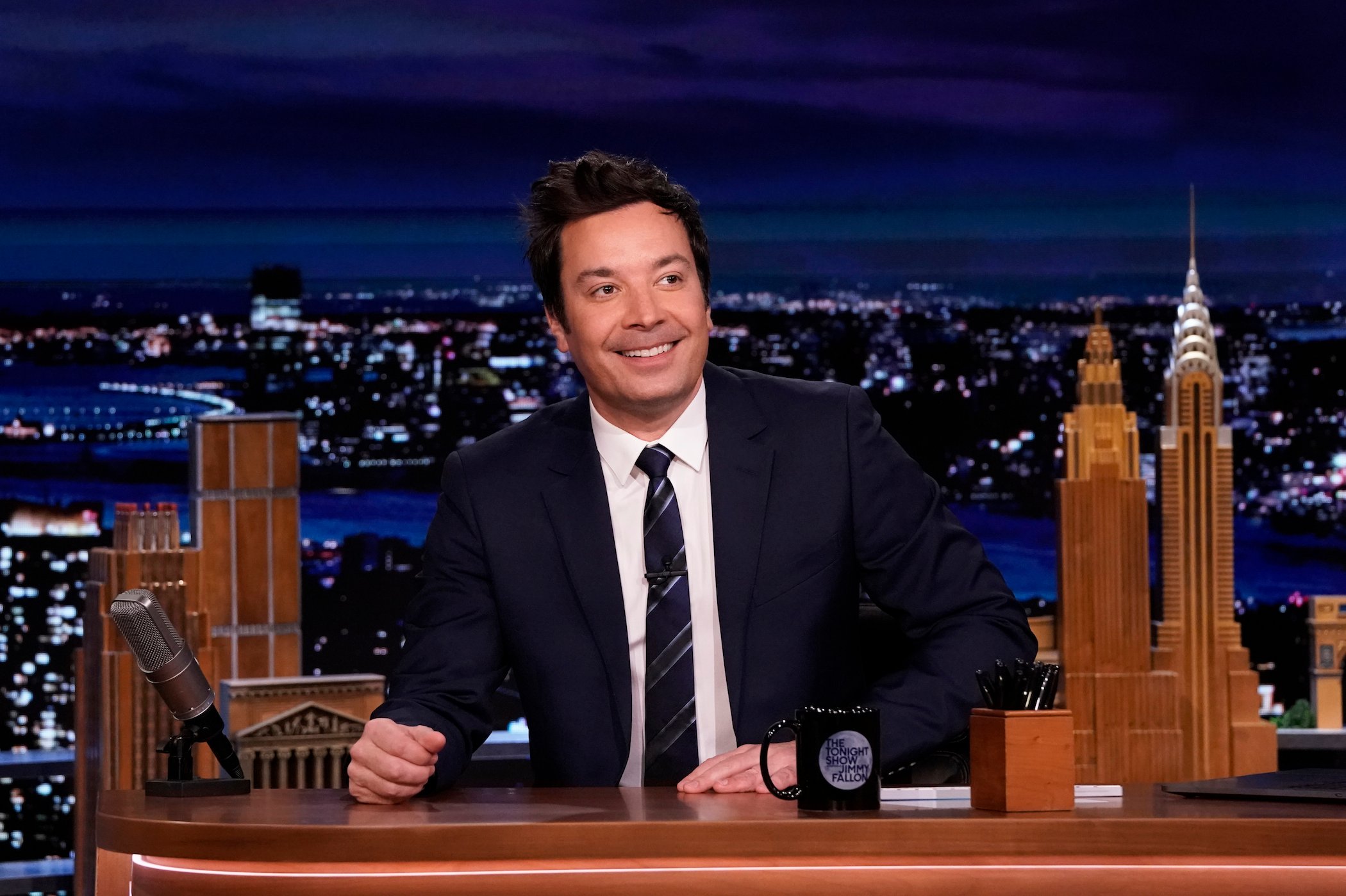 Jimmy Fallon smiling and sitting at his desk on 'The Tonight Show Starring Jimmy Fallon,' where he accrues an incredible net worth