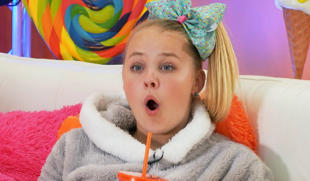 JoJo Siwa wearing a bright blue bow reacts to a TV show