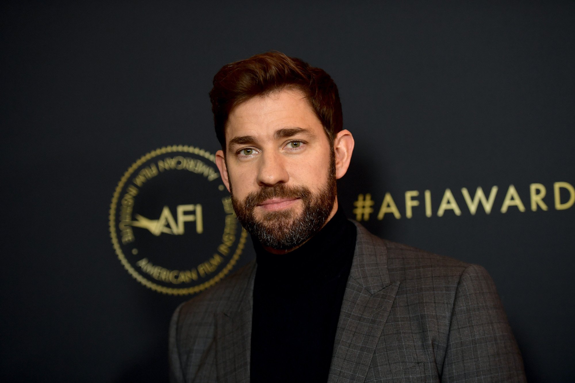 John Krasinski smiling in front of a black background