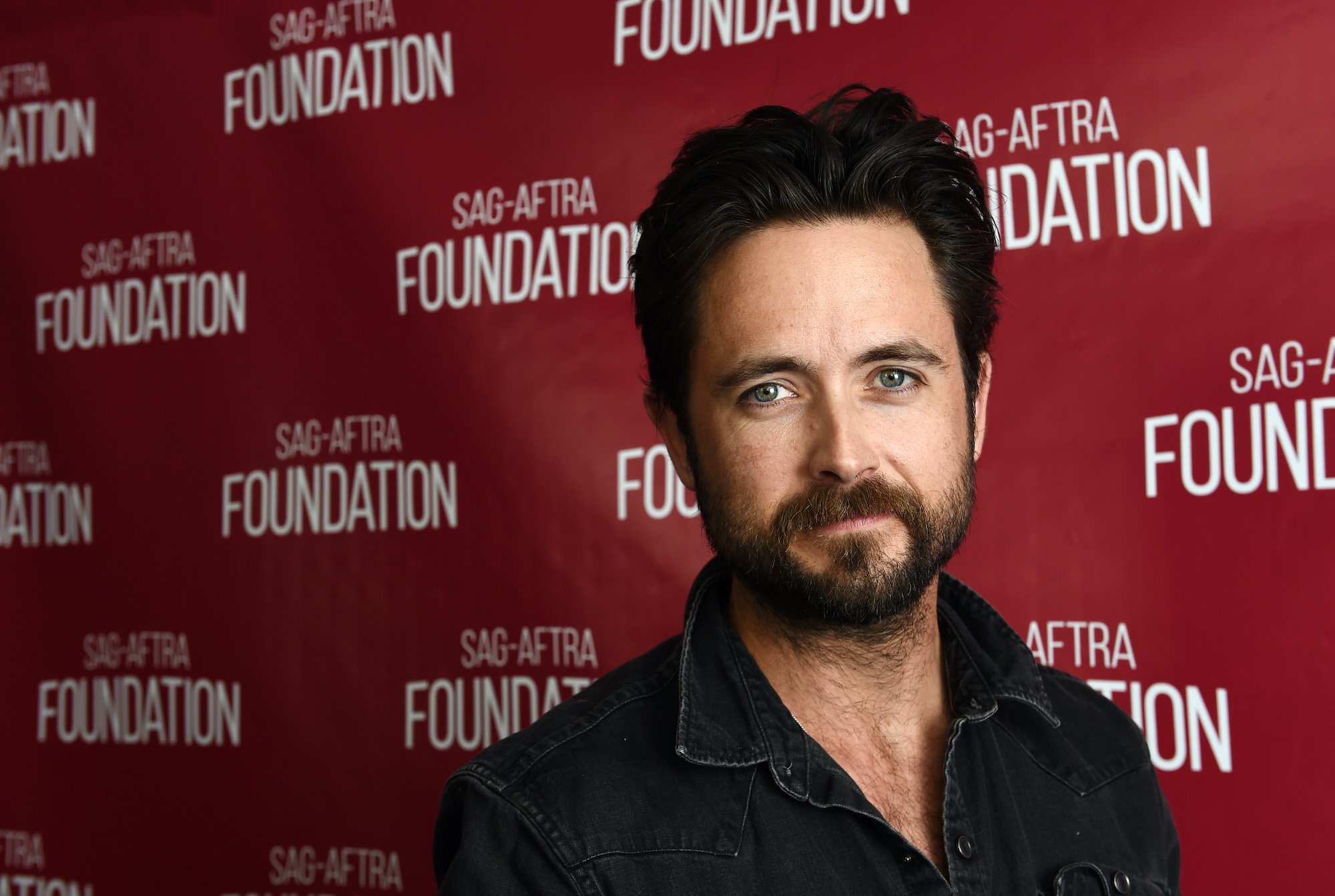 Justin Chatwin smiling in front of a red background
