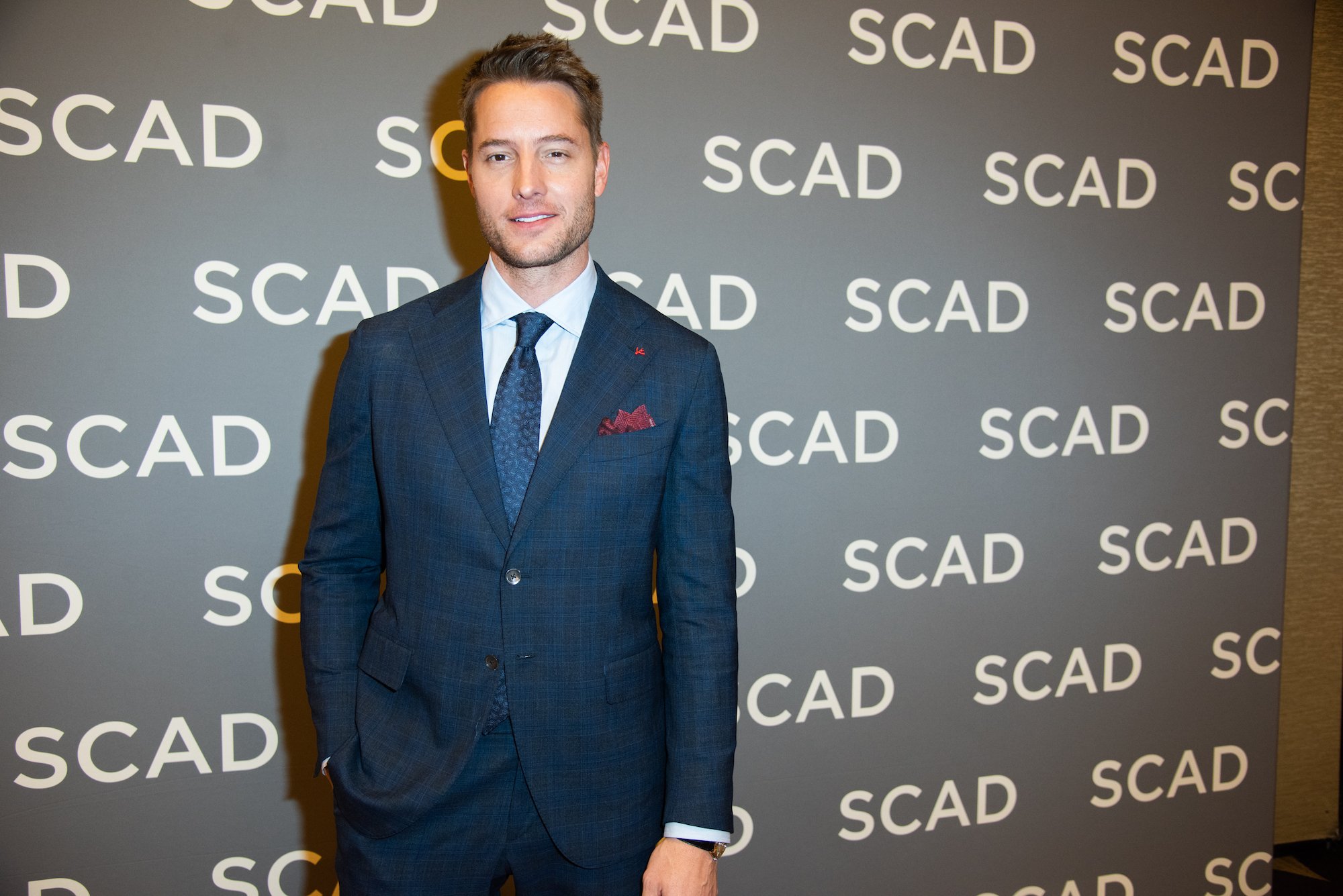 Justin Hartley smiling in front of a gray background