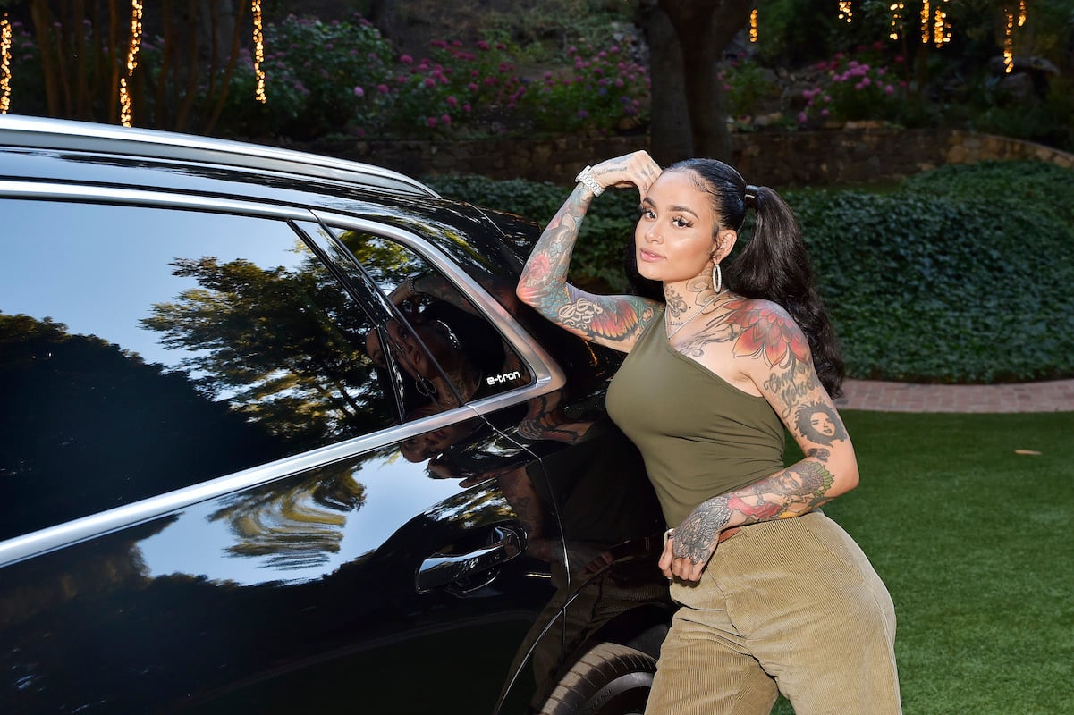 Kehlani poses in front of a black car wearing a green one-shoulder top and green pants with her hair in a ponytail