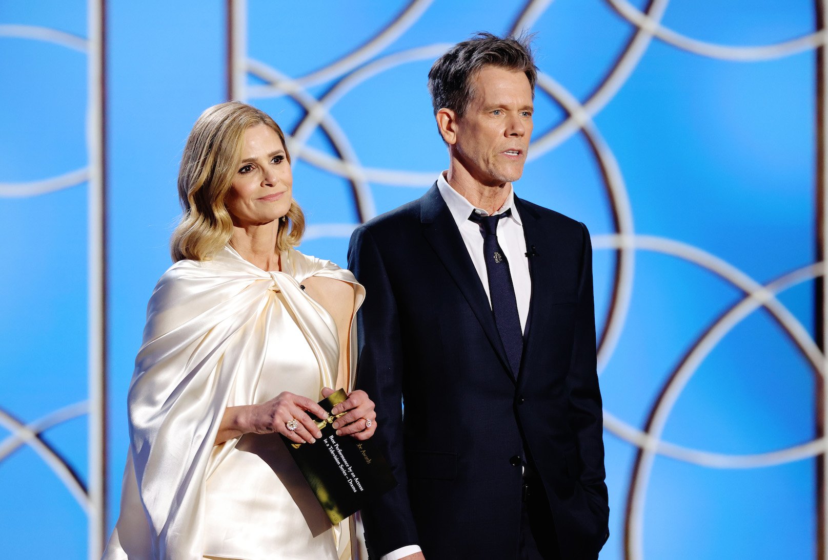 Kyra Sedgwick and Kevin Bacon standing next to each other speaking onstage at the 78th Annual Golden Globe Awards