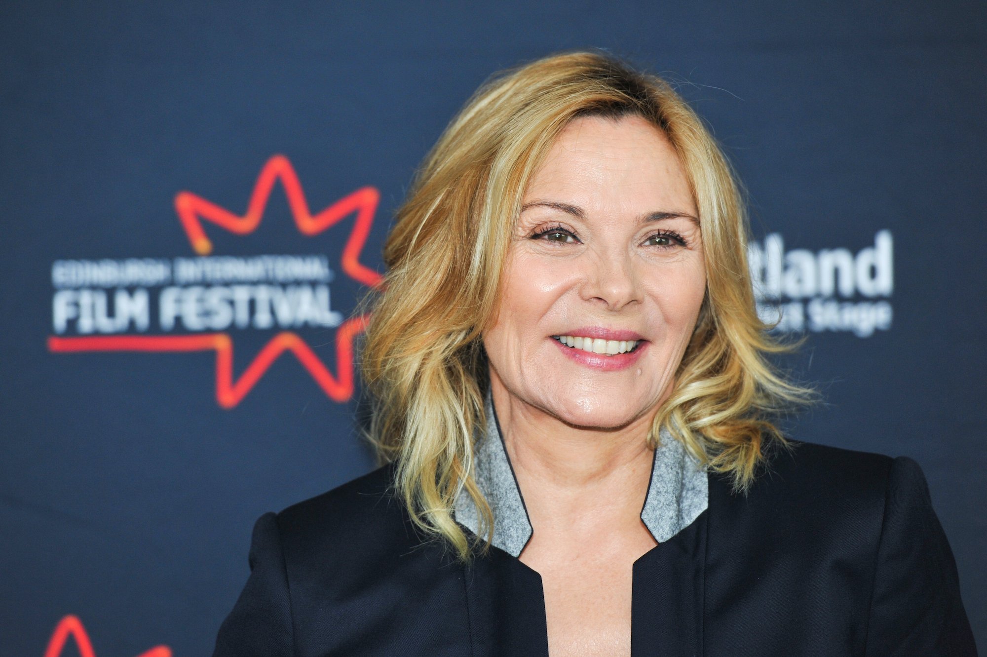 Kim Cattrall smiling in front of a blue background
